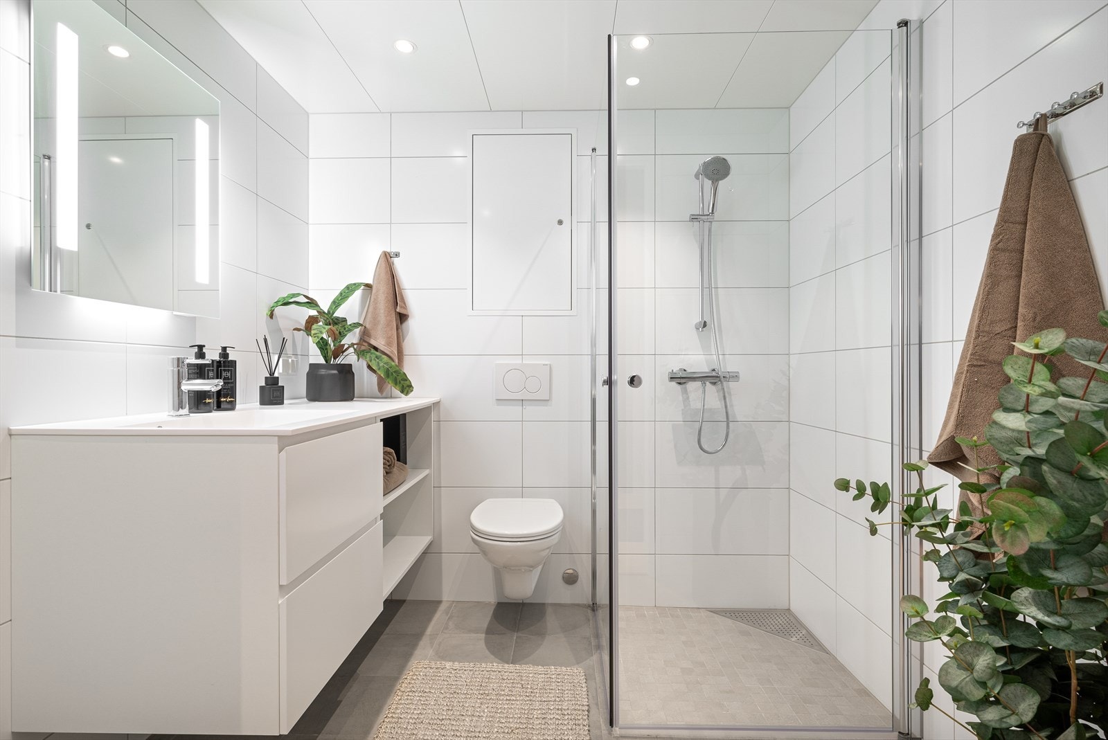 Badet er på 4,5 kvm., og har flislagt gulv med varmekabler, flislagte vegger, vegghengt wc, dusjhjørne med sammenslåbare dusjdører og spotter i tak. Galleribilde