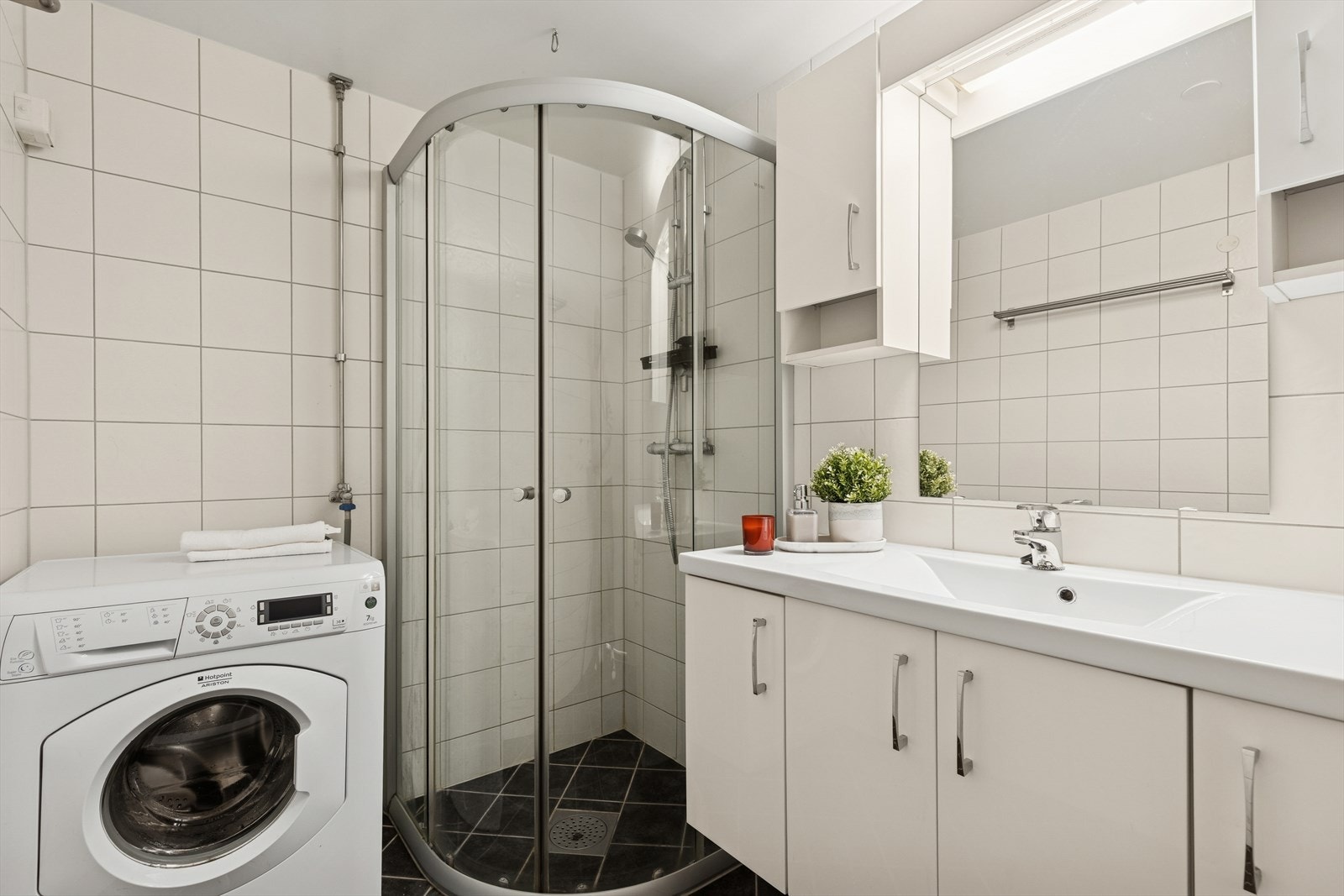 Badet er innredet med dusj direkte på gulv med dusjvegger, nedfelt servant med tilhørende skapløsning under, samt speil, belysning og overskap over servanten. Galleribilde