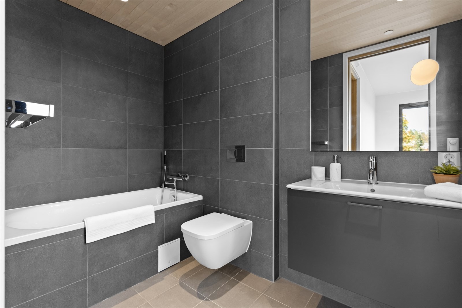 Lekkert baderom med direkte adkomst fra soverom. Innebygget badekar, vegghengt toalett og servantskap med stort speil over. Galleribilde