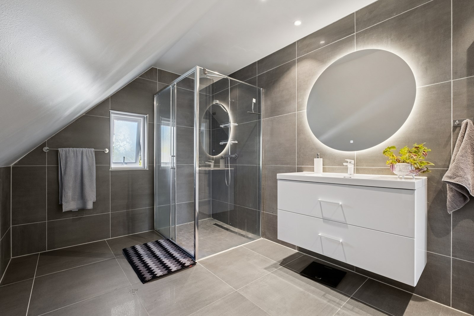 Badet er utstyrt med vegghengt toalett, dusjhjørne med glassdører, samt baderomsinnredning med heldekkende servant og speil. Galleribilde