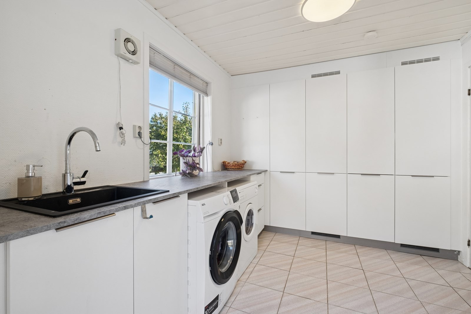 Romslig vaskerom som er praktisk innredet med store veggskap, innredning med benkeplate og utslagsvask, samt opplegg for vaskemaskin. Galleribilde