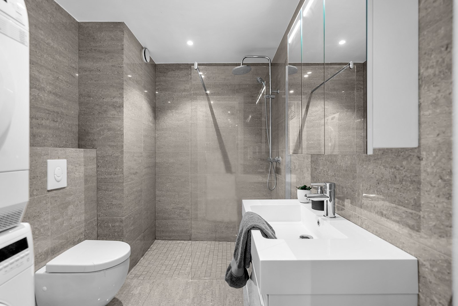 Eksklusivt helfliset baderom som kombinerer funksjonalitet og stil på en elegant måte. Rommet har en dusjnisje med fossefallsdusj og en trendy glassvegg. Speilskap med integrert belysning for optimal komfort. Servanten har praktiske underskuffer. Galleribilde