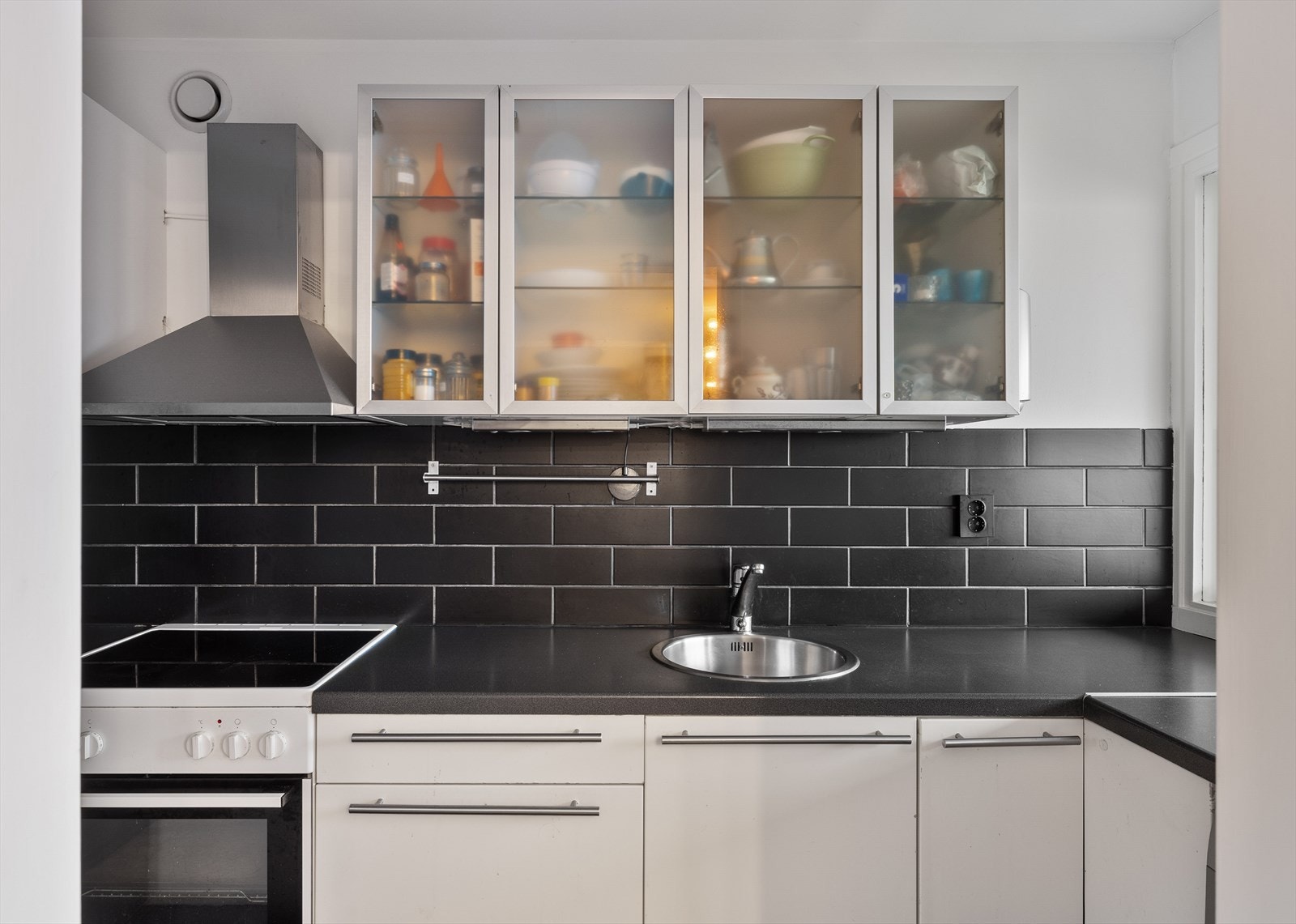 Kjøkken med mørke fliser, god benkeplass og praktiske overskap med glassfronter. Galleribilde