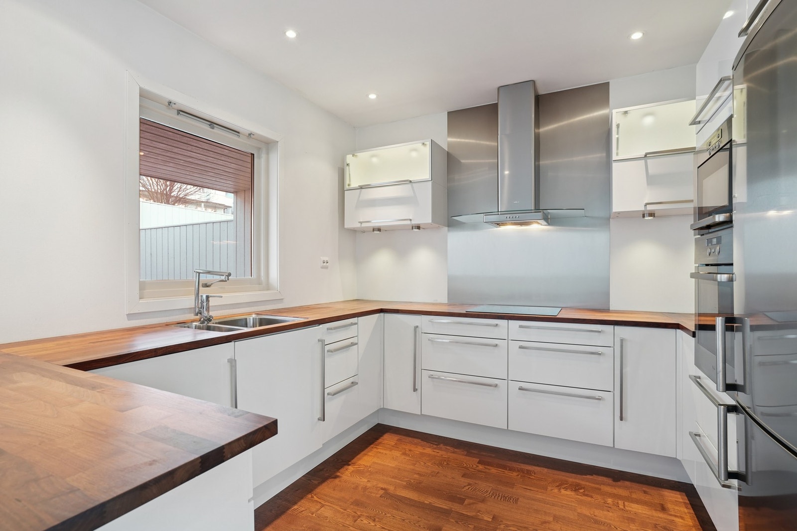 Kjøkkeninnredning med lyse glatte fronter og håndtak. Belysning under overskap. Galleribilde