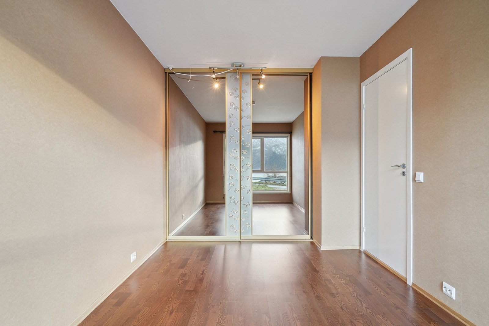 Det er montert skyvedørsgarderobe med speildører. På gulvet er det parkett og på veggene er det tapet. Galleribilde