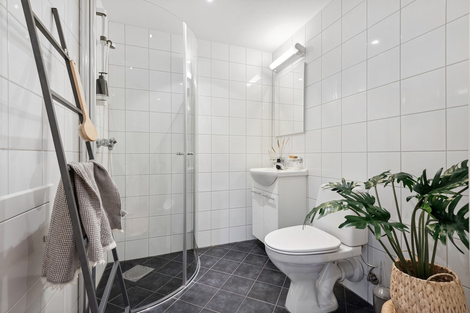 Badets areal er like velutnyttet som i resten av leiligheten. Dusjhjørnets buede glassdører kan svinges inn. I hjørnet innenfor døren er det plass til vaskemaskin. Galleribilde