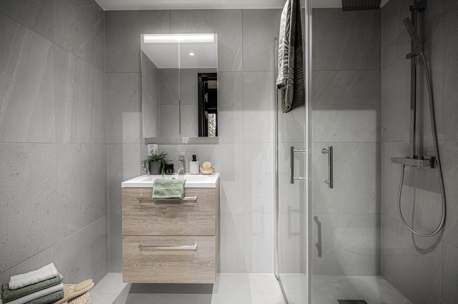 Baderomsinnredningen fra Bano Home med hvit heldekkende servant, speilskap med lys i toppen av dørene, vegghengt toalett med softclose, spyleknapp fra Blank krom, dusjvegger, servantarmatur fra Grohe Eurocube og dusjsett fra Grohe Eurocube. Galleribilde