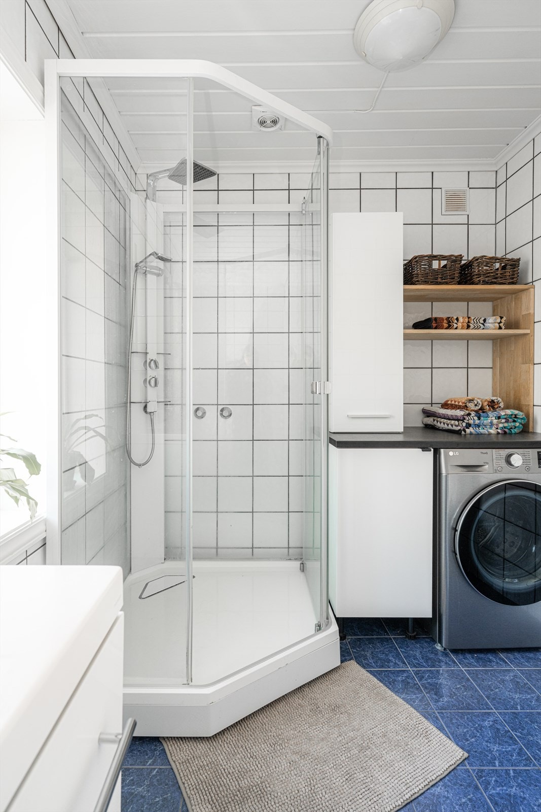 Badet inneholder gulvmontert toalett, dusjkabinett, servant med underskap, speil med lys og opplegg til vaskemaskin. Galleribilde