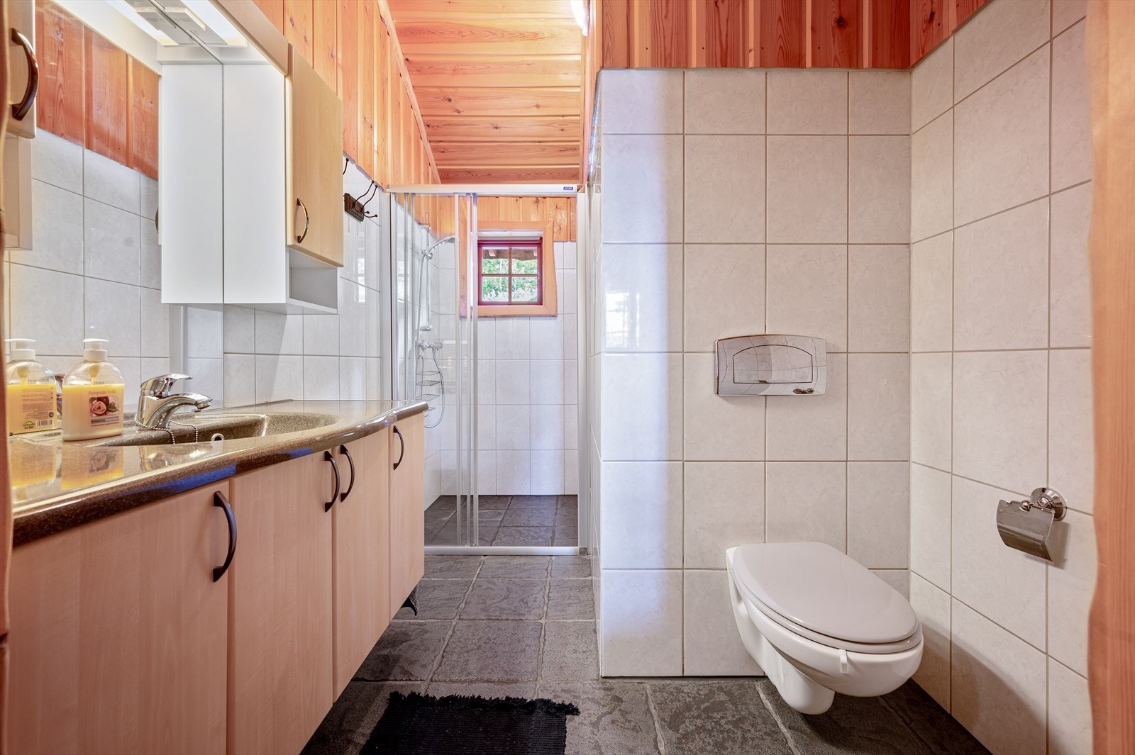 Innredningen består av servant, speil, veggehengte skap, veggmontert toalett og dusjhjørne Galleribilde