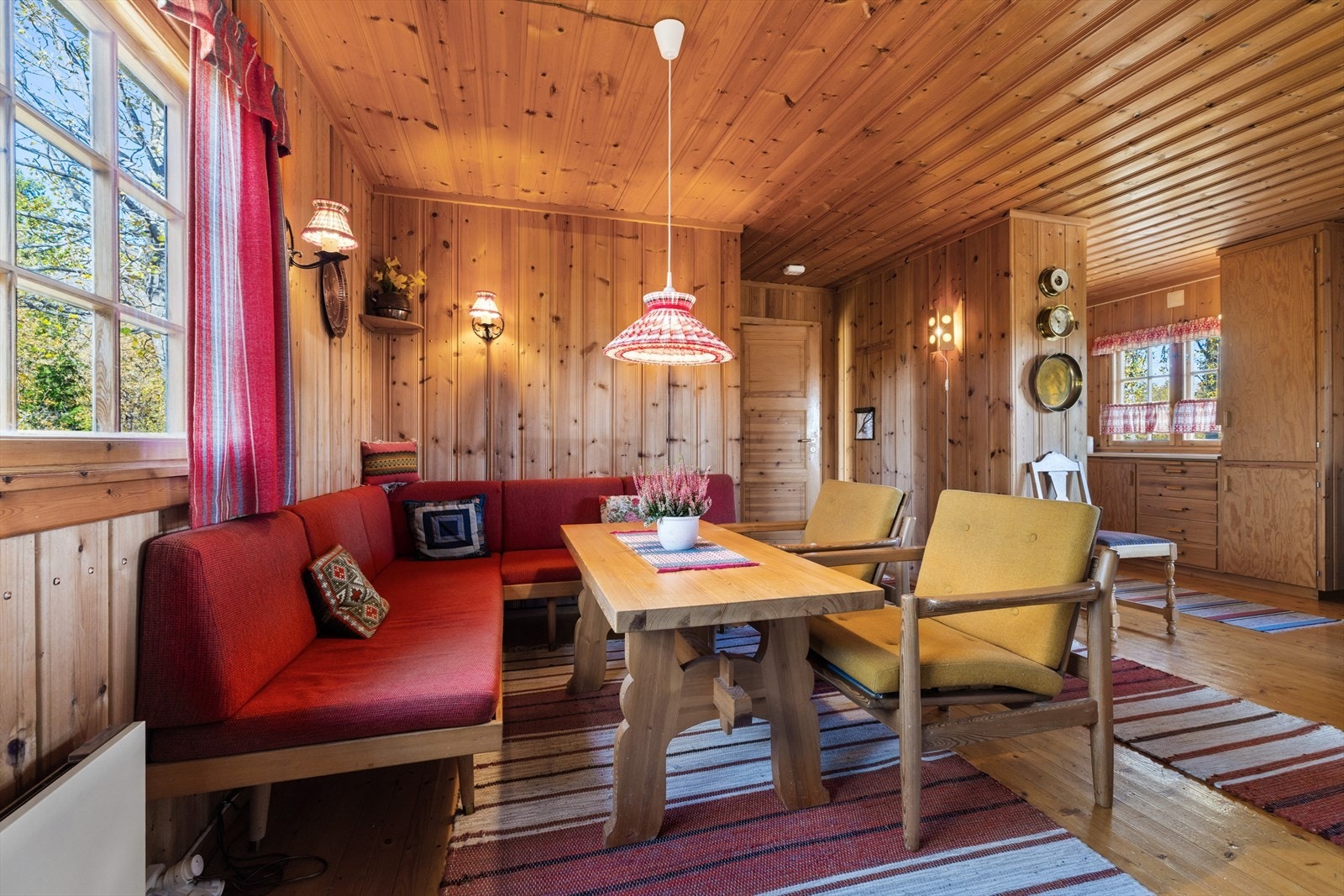 Romslig stue med lun atmosfære, trepanel på vegger og tak, store vinduer som slipper inn naturlig lys. Galleribilde