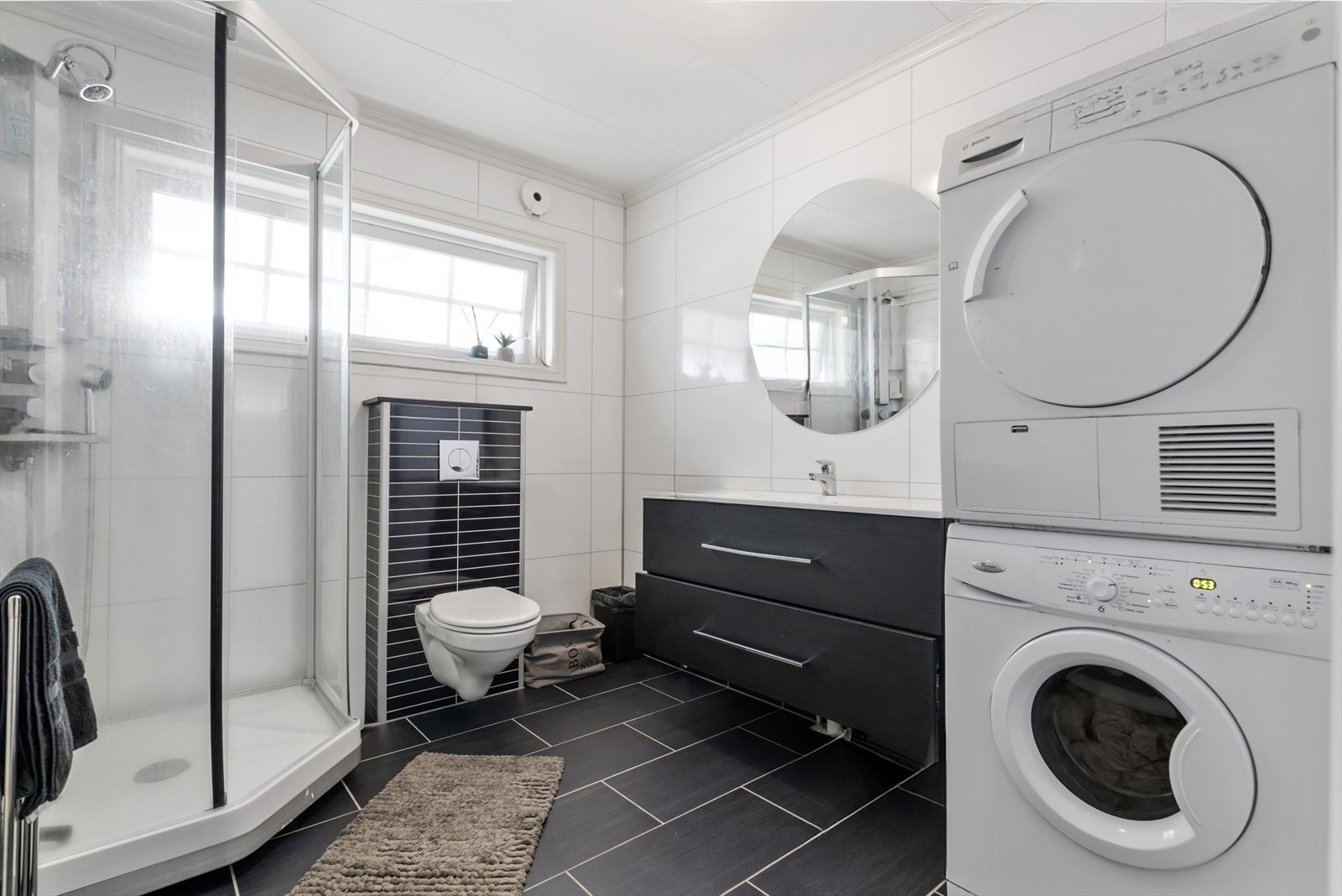 Bad/vaskerom i hovedetasjen har flislagt gulv og våtromsplater på vegg | rommet er utstyrt med dusjkabinett, vegghengt wc, baderomsinnredning og opplegg for vaskemaskin og tørketrommel Galleribilde