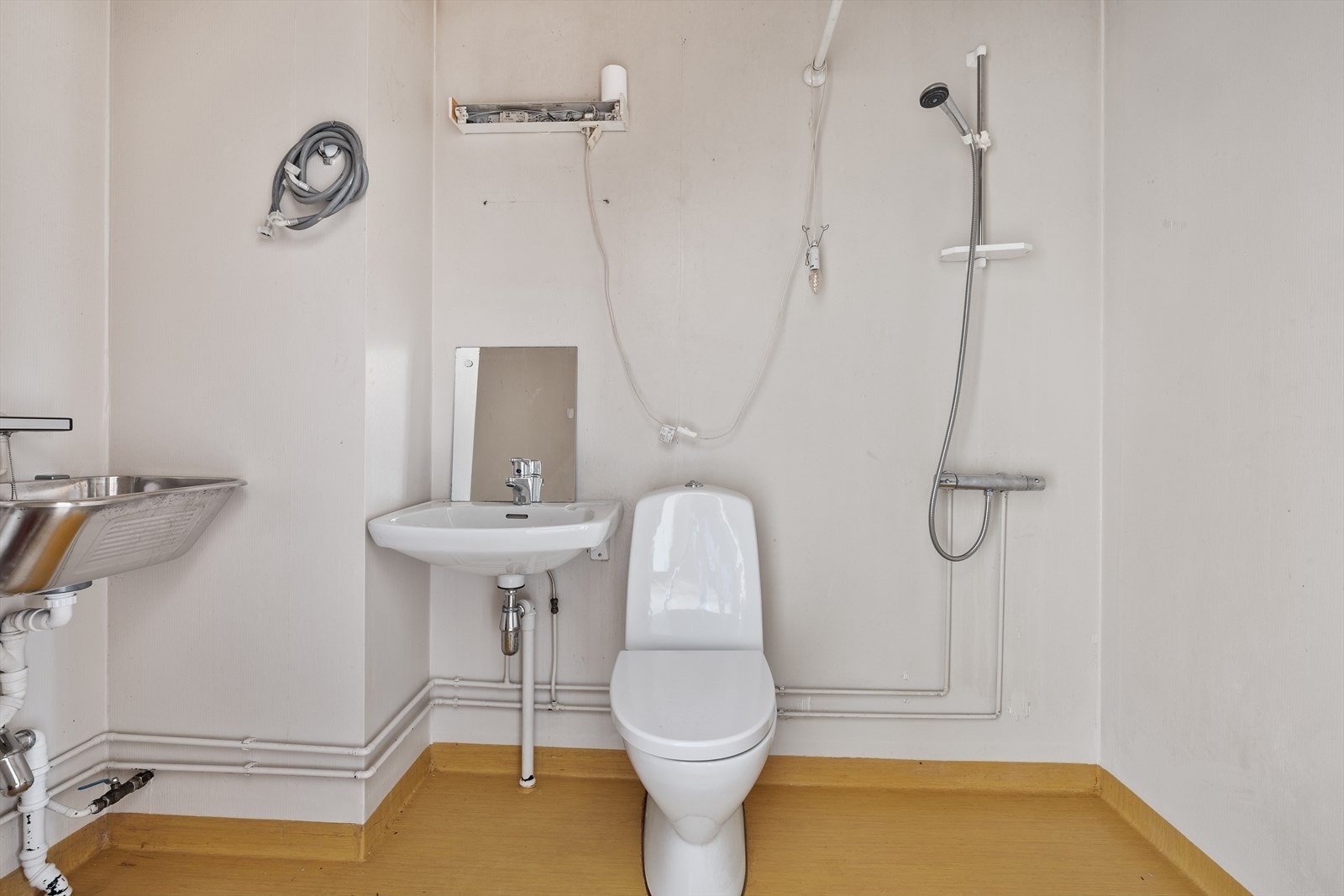 Bad med vinylbelegg på gulvet, malt tapet på vegger, og malt slett tak. Rommet er innredet med servant, utslagsvask, dusjhjørne og opplegg for vaskemaskin. Rommet må renoveres. Galleribilde