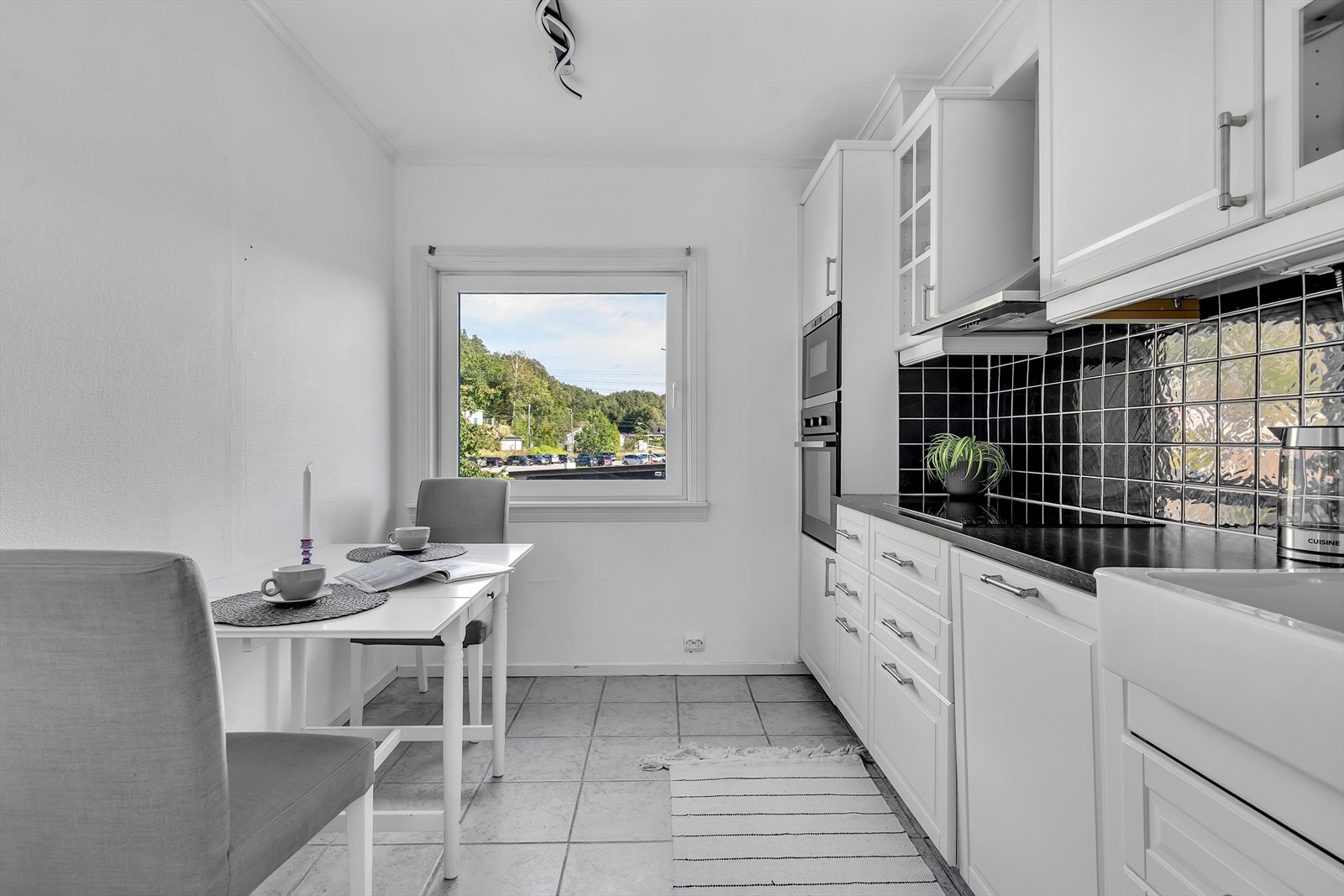 De integrerte hvitevarene - i form av platetopp, stekeovn og praktisk mikrobølgeovn i ståhøyde samt oppvaskmaskin - bidrar til et sømløst og stilrent helhetsinntrykk. Pene detaljer som fliser over kjøkkenbenken og keramisk vask. Galleribilde