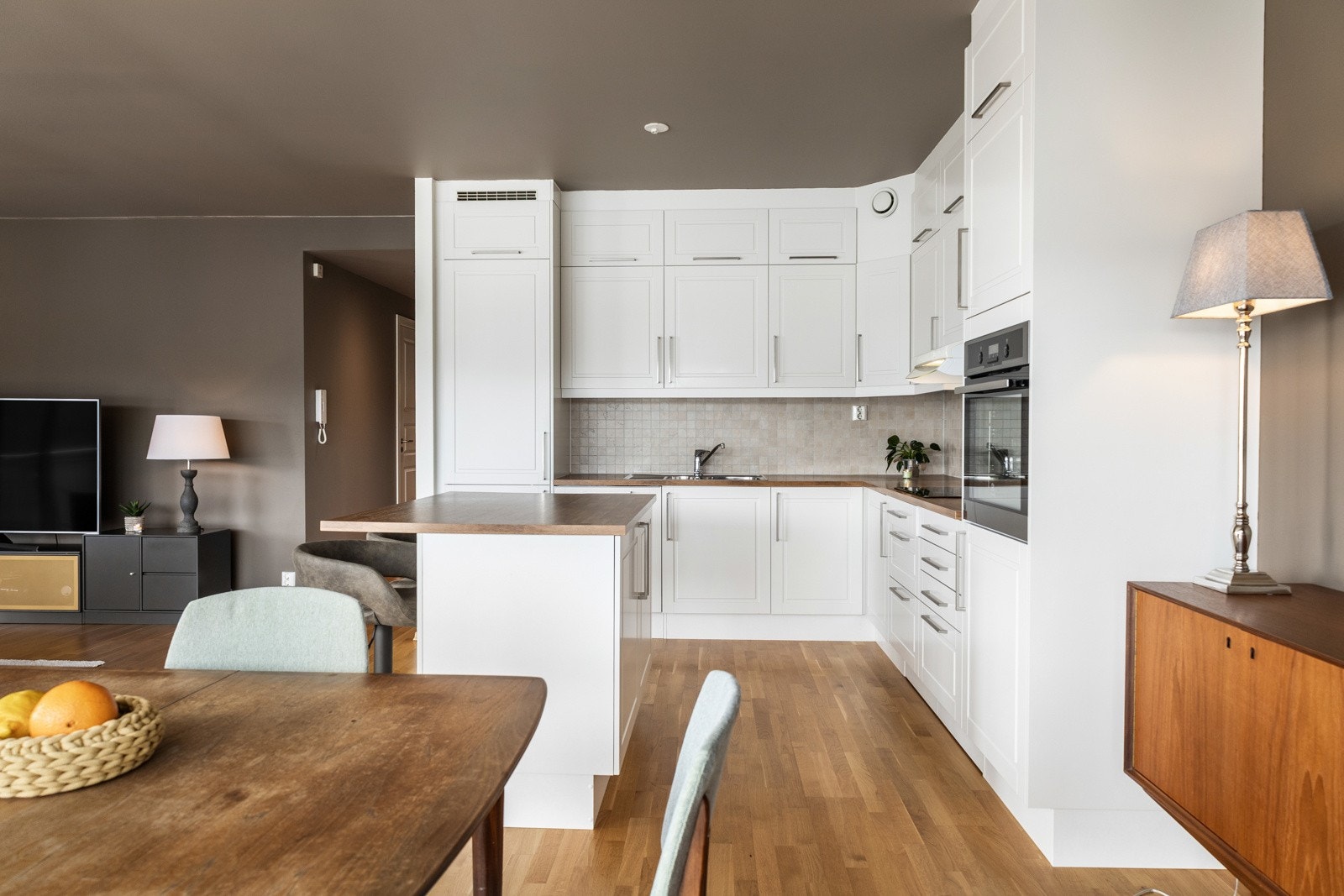 Lyst kjøkken med moderne hvite skap, integrerte hvitevarer og en praktisk kjøkkenøy. Åpen løsning mot stue. Galleribilde