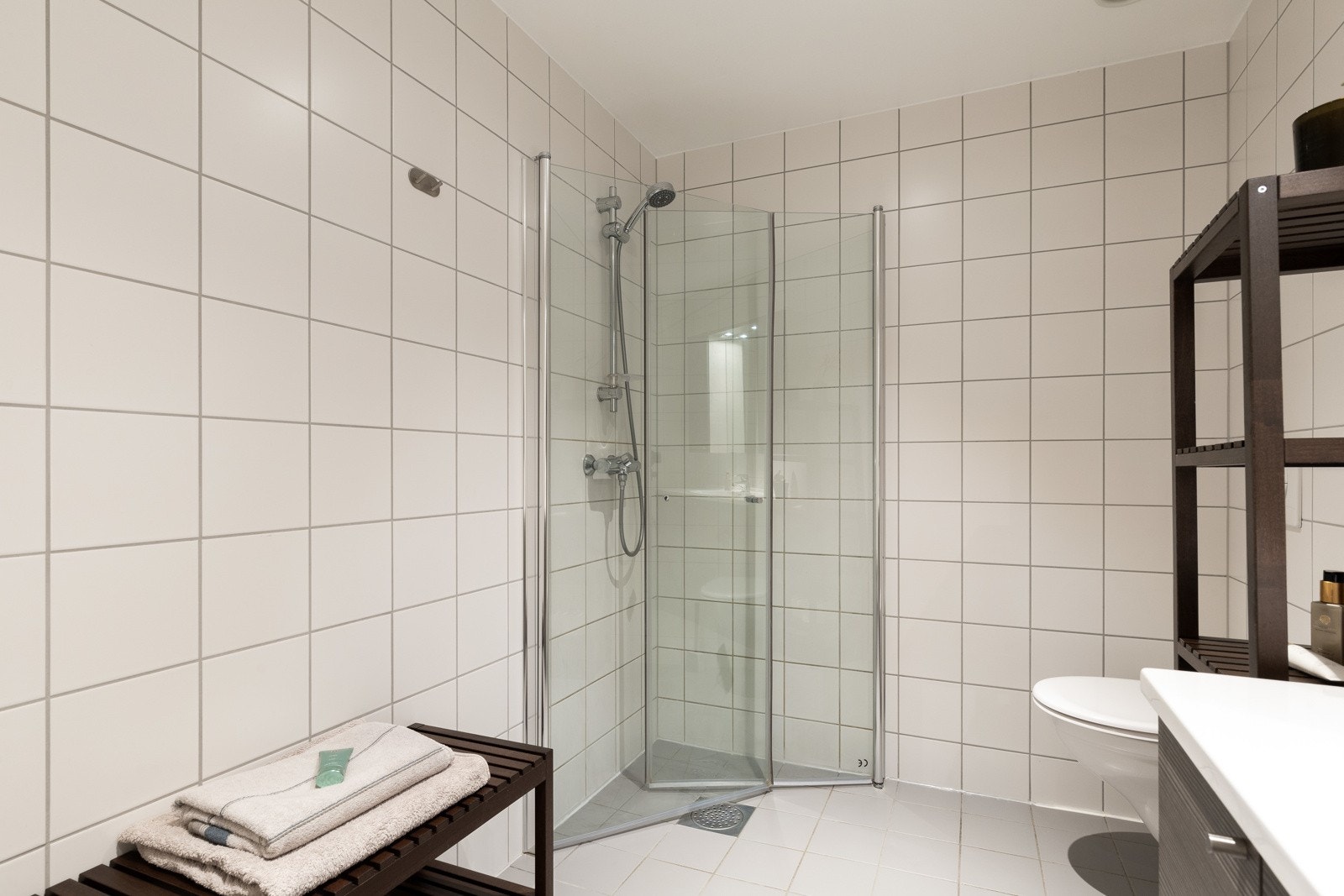 Lyst flislagt baderom med dusj, servant og toalett. Galleribilde