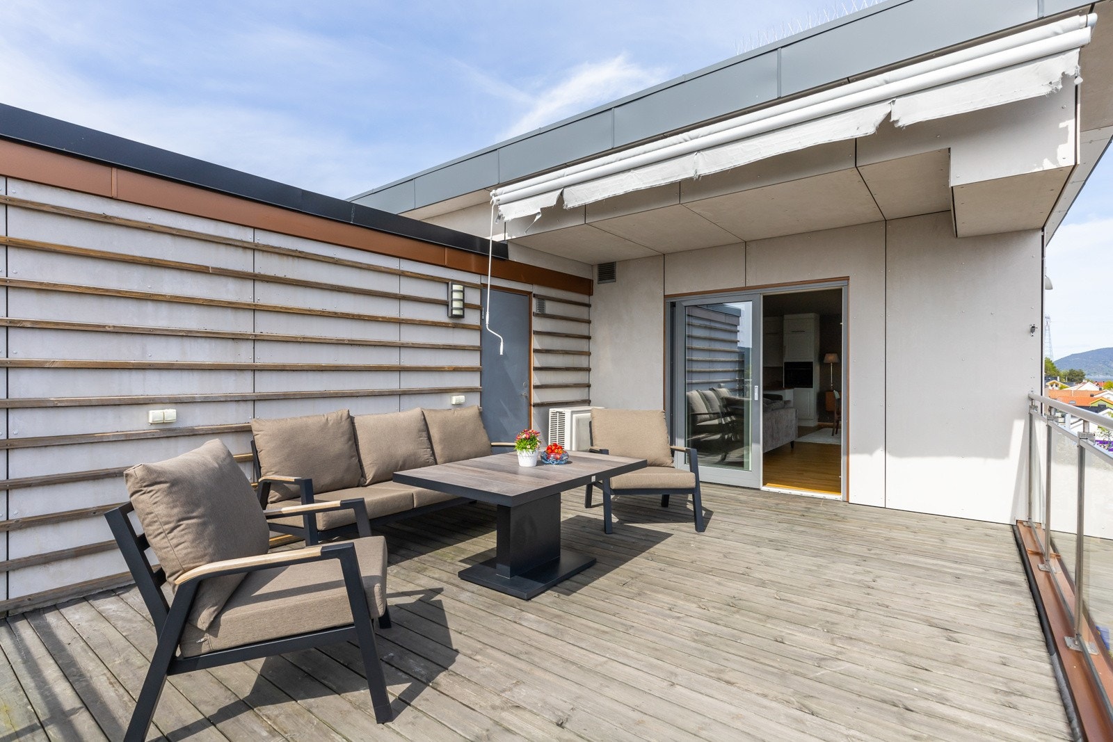 Romslig terrasse med sittegruppe og bord, markise over sitteplassen og skyvedør inn til boligen. Galleribilde