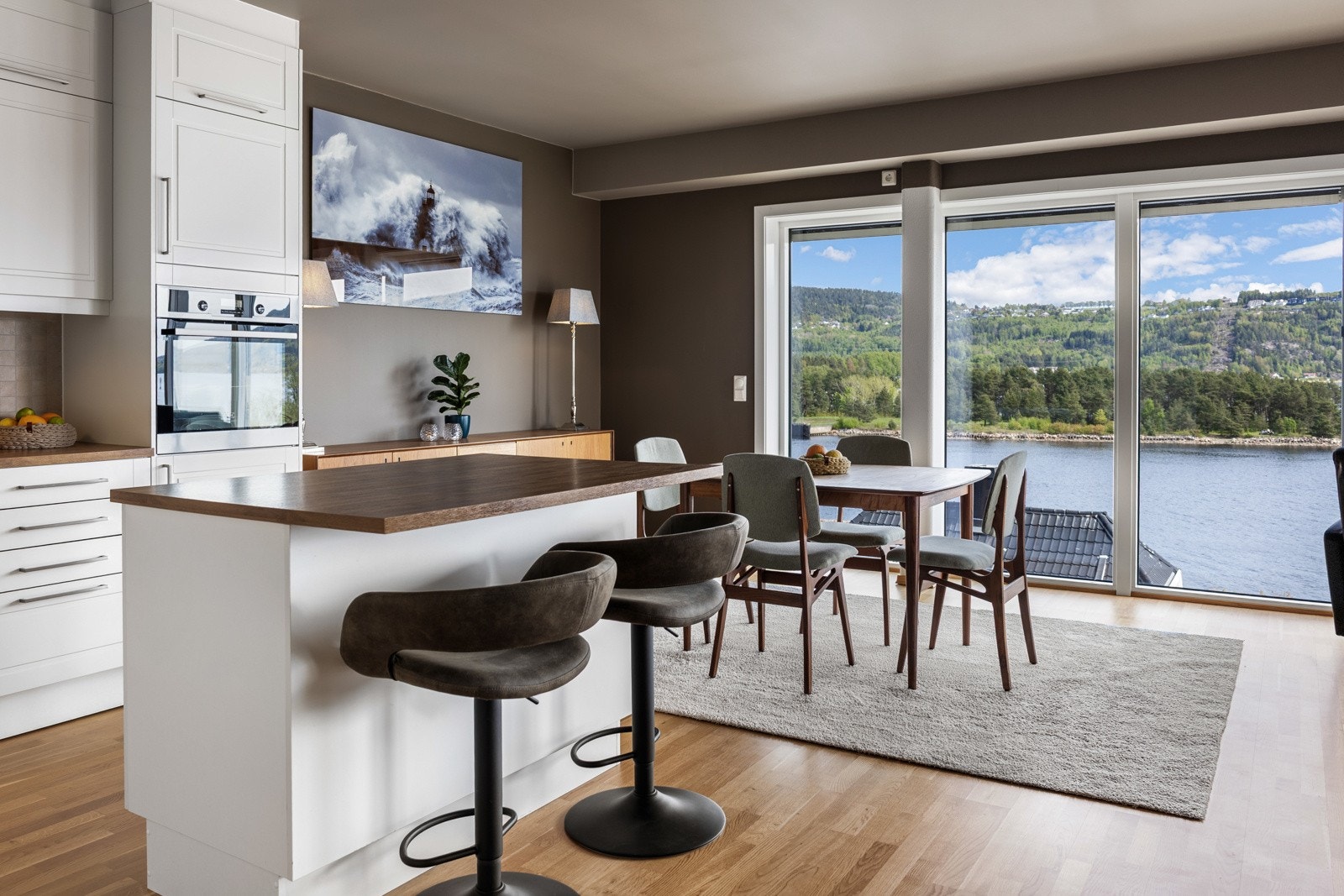 Kjøkken med spiseplass og store vinduer som gir utsikt over fjorden og grønt landskap. Galleribilde