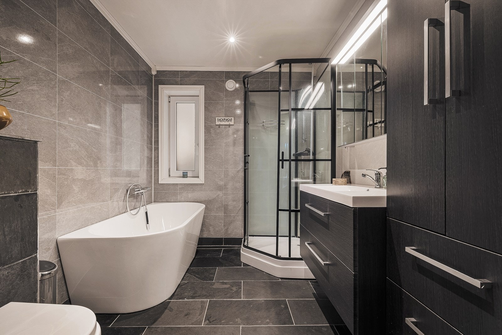 Badet rommer 6,1m² og har samme fliser som i entréen. Badet er utrustet med både badekar og et romslig dusjkabinett, og er oppvarmet med varmekabler i gulv Galleribilde