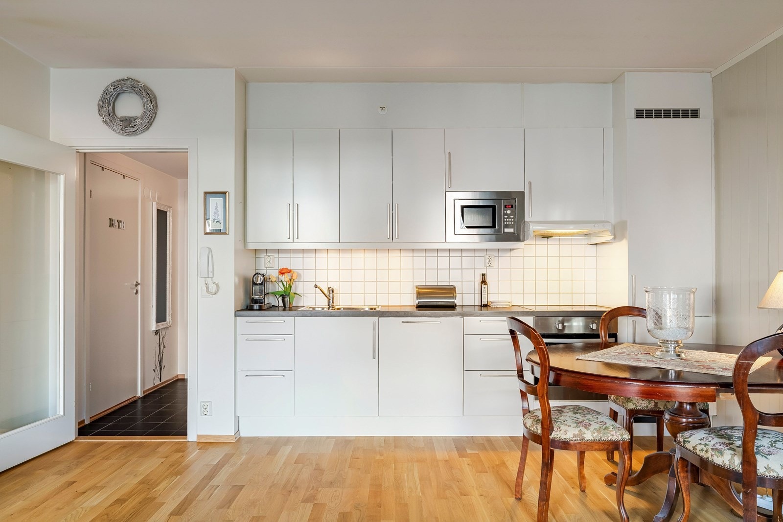 Kjøkkeninnredningen har et enkelt og moderne uttrykk med hvite, slette fronter og mørk benkeplate i laminat. Det er integrert platetopp, mikrobølgeovn, stekeovn og ventilator, og løsningen gir god arbeidsflate og skapplass. Galleribilde