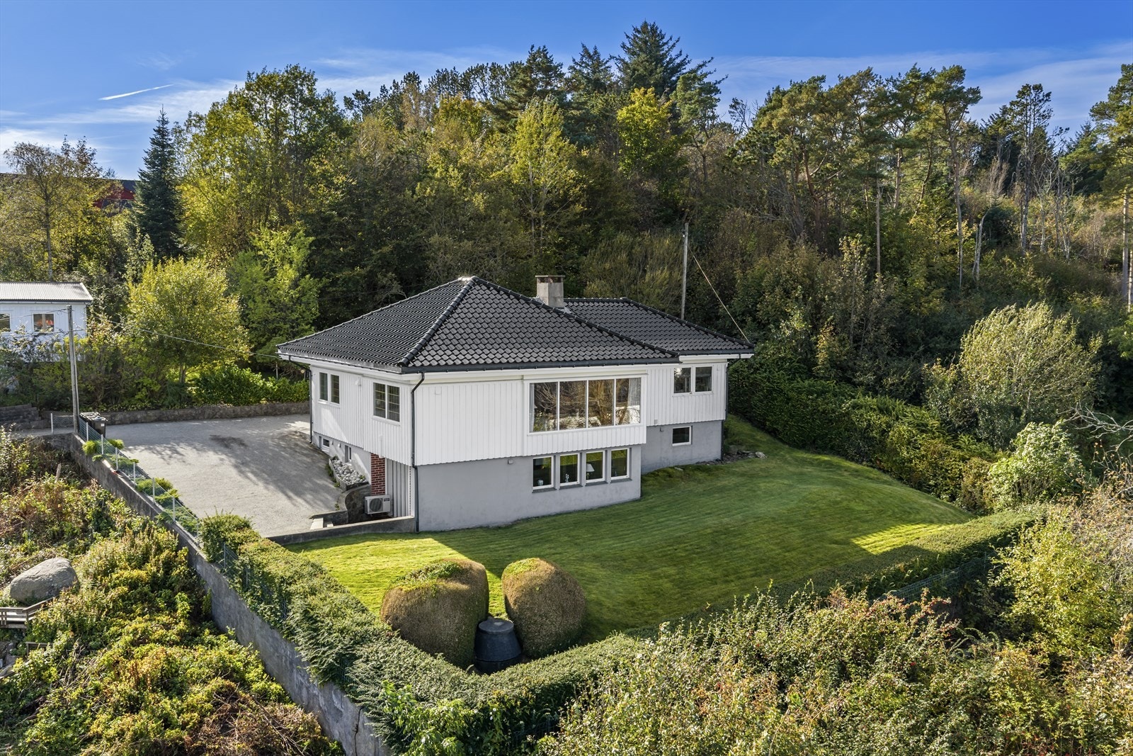 Tomten er pent opparbeidet med asfaltert innkjørsel/gårdsrom, ellers beplantet med plen, trær, busker og bed. Galleribilde