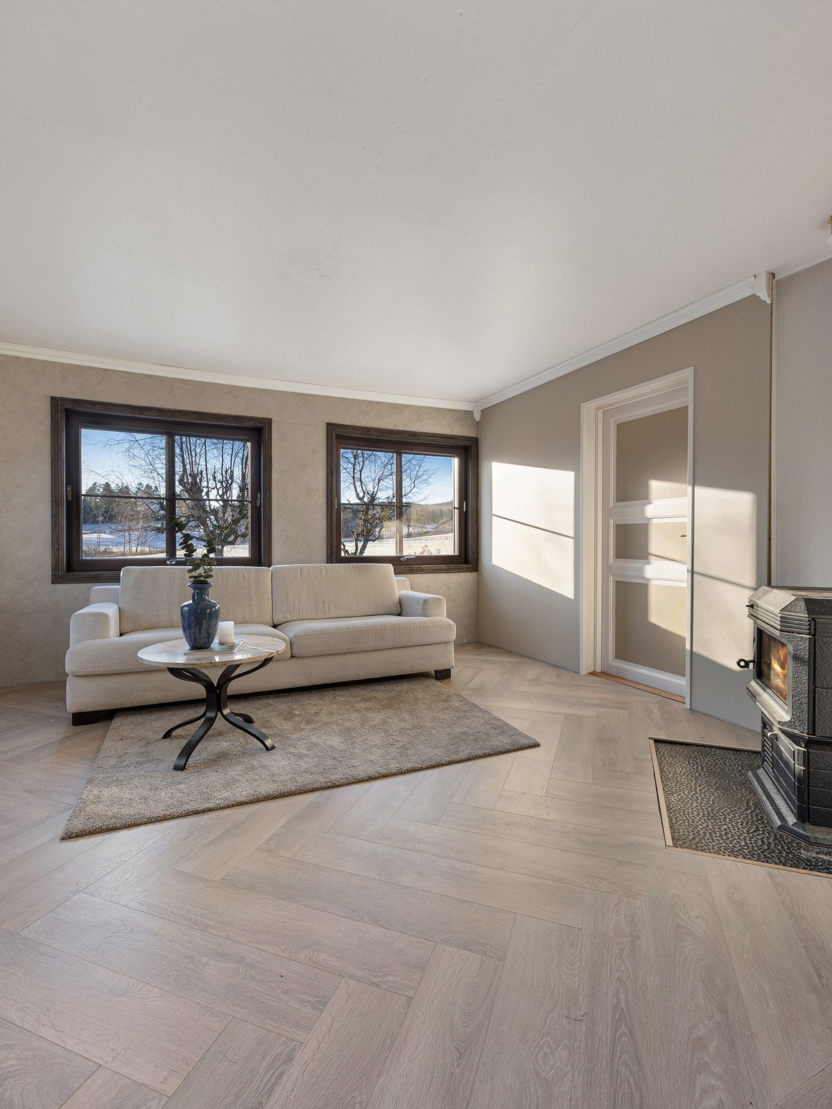 Hovedstuen får lys fra to sider, og vinduene inkluderer en glassdør til terrassen. Utsikten er grønn og landlig, og lune kvelder sikres av en vedovn i hjørnet. Galleribilde