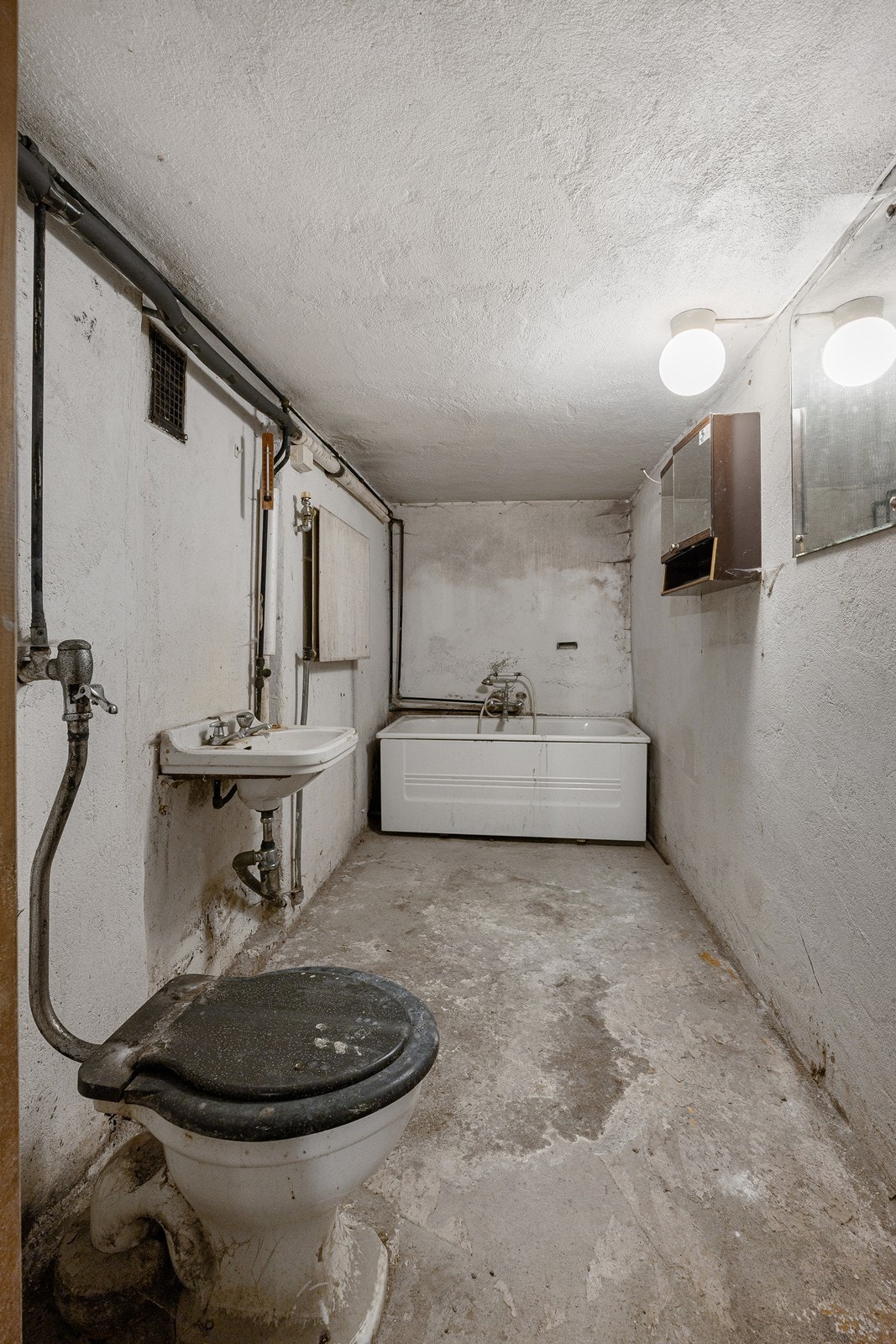 Kjellerbadet har enkel standard med eldre overflater av betong. På badet er det toalett, servant og badekar. Galleribilde