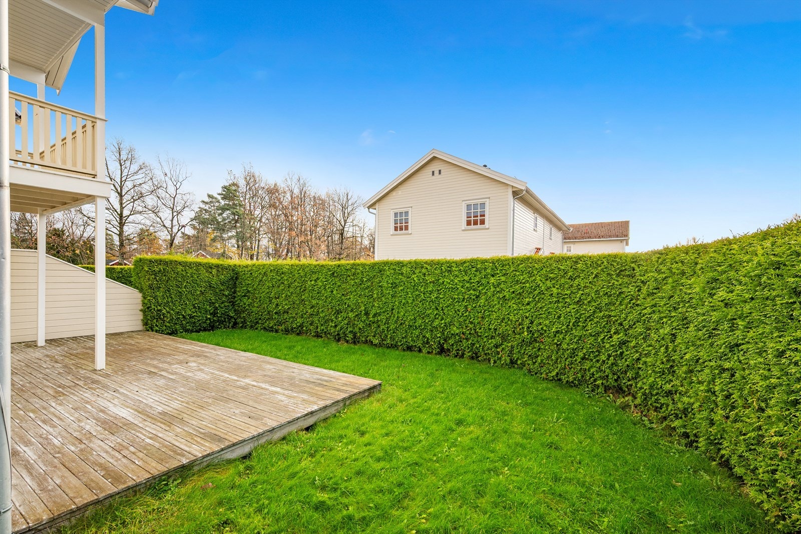 Pent og usjenert uteområde med hekk, gressplen og terrasse og balkong Galleribilde