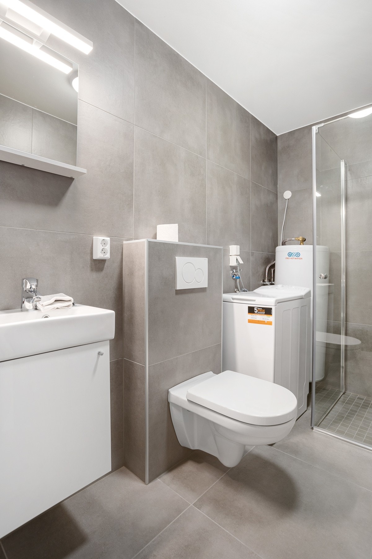 Flislagt baderom med vegghengt toalett, baderomsinnredning og vaskemaskin. Galleribilde