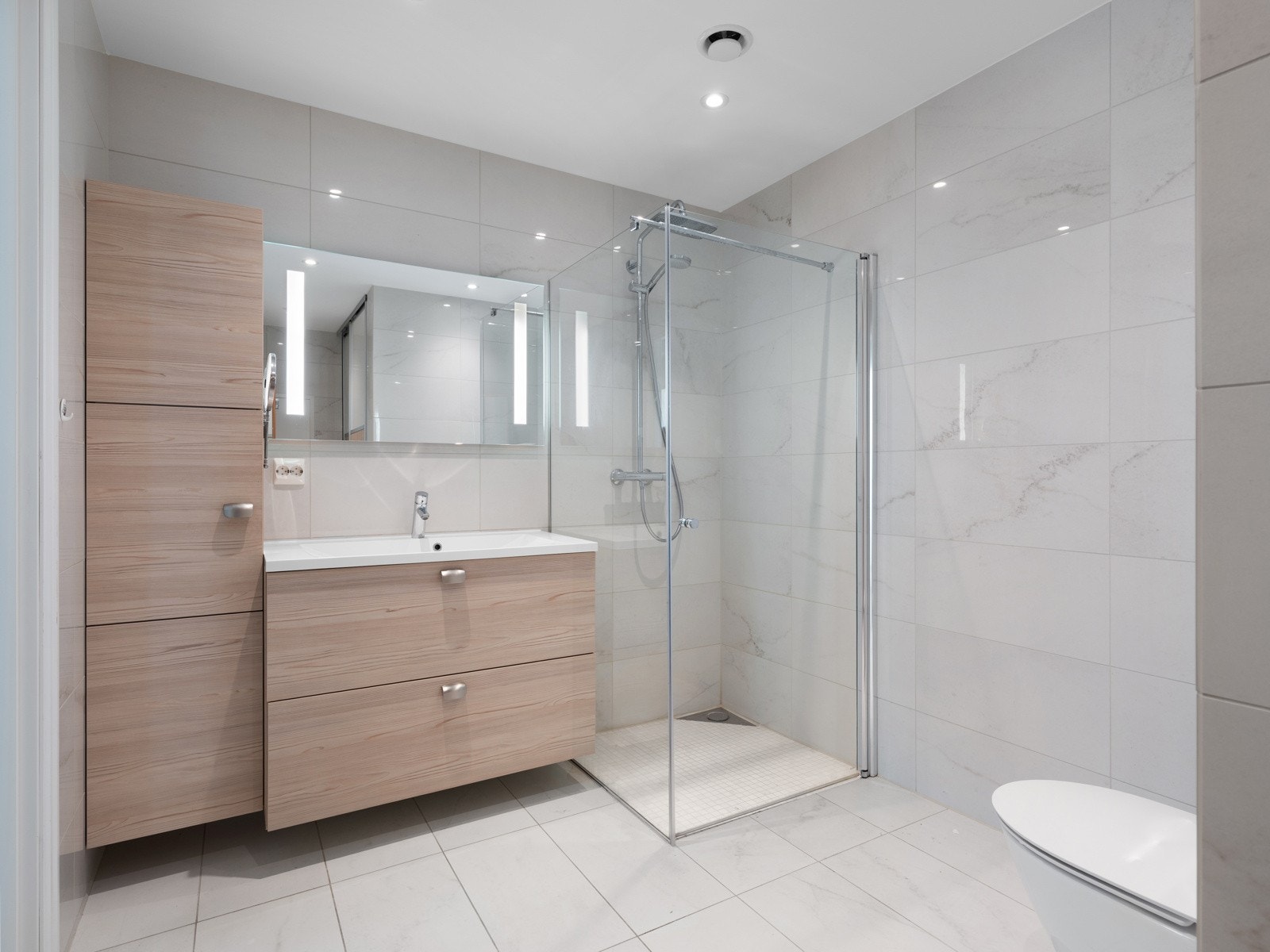 Badet er helfliset og har en moderne innredning med speil og skuffer som gir gode oppbevaringsmuligheter. Galleribilde