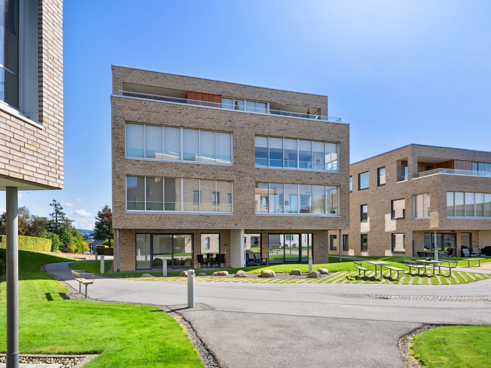 Boligens fellesarealer er godt tilrettelagt med grønne plener, asfalterte stier og flere sittebenker. Galleribilde