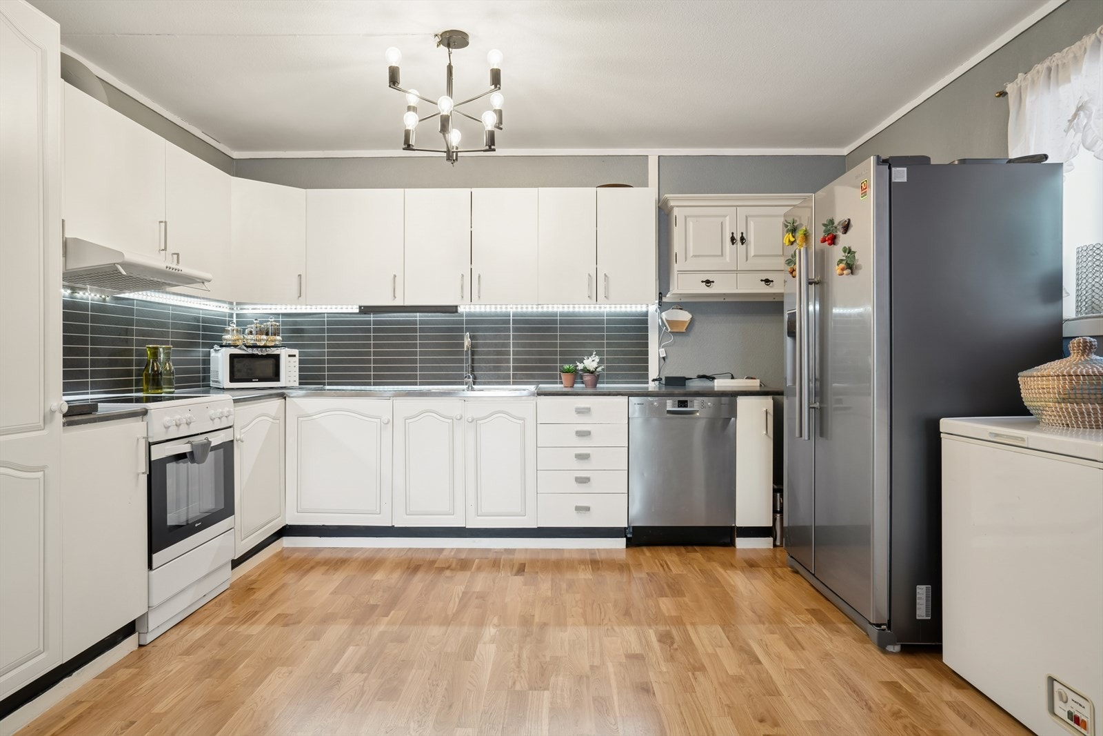 Kjøkkenet har innredning med hvite profilerte fronter, laminert benkeplate med nedfelt kjøkkenvask i stål og Kitchenboard på vegg over benk Galleribilde