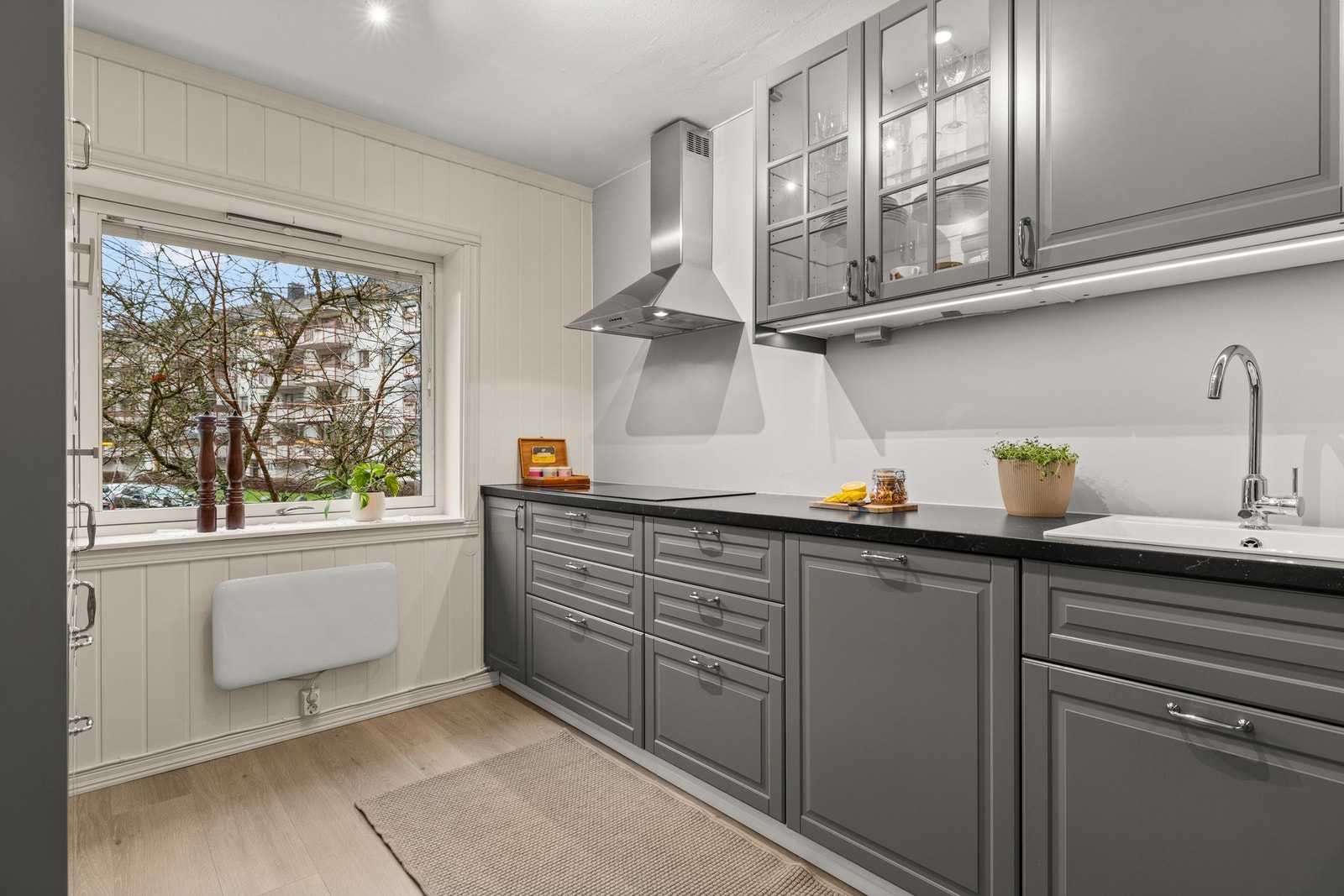 Pen IKEA kjøkkeninnredning fra 2016, med profilerte fronter. Dobbelt vitrineskap med glasshyller og belysning. Galleribilde