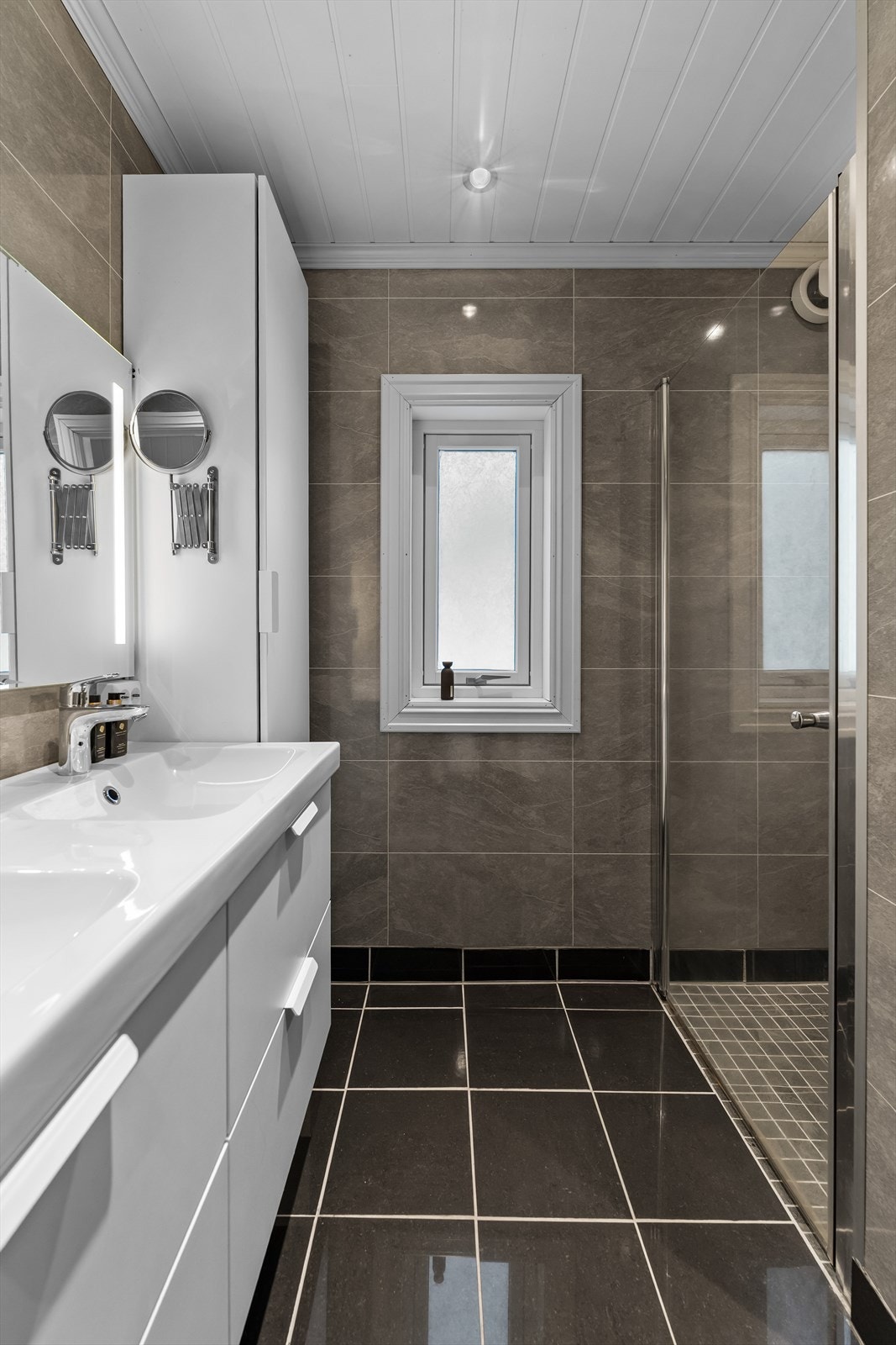 Helfliset baderom i naturtoner fra 2019 - Innredning med skuffer under dobbel servant, høyskap og speil med integrert belysning. Galleribilde