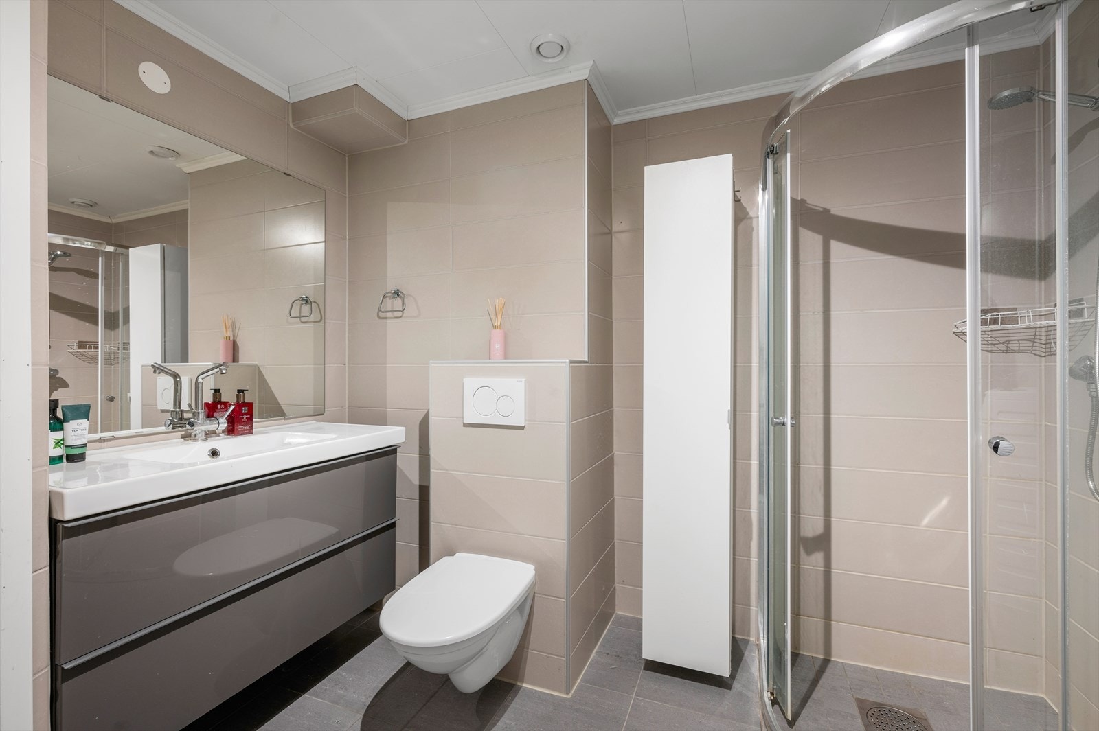 Badet er utstyrt med dusjhjørne, mekanisk avtrekk, opplegg for vaskemaskin, servant, servantskap og veggmontert wc. Galleribilde