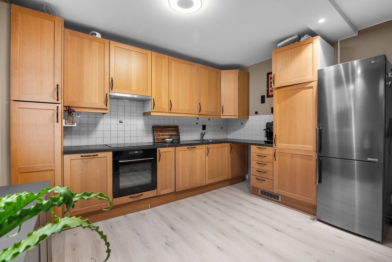 Funksjonelt kjøkken med profilerte fronter, nedfelt oppvaskkum og integrert platetopp/ovn. Flislagt vegg og kullfilterventilator gir et praktisk og tidløst uttrykk. Galleribilde