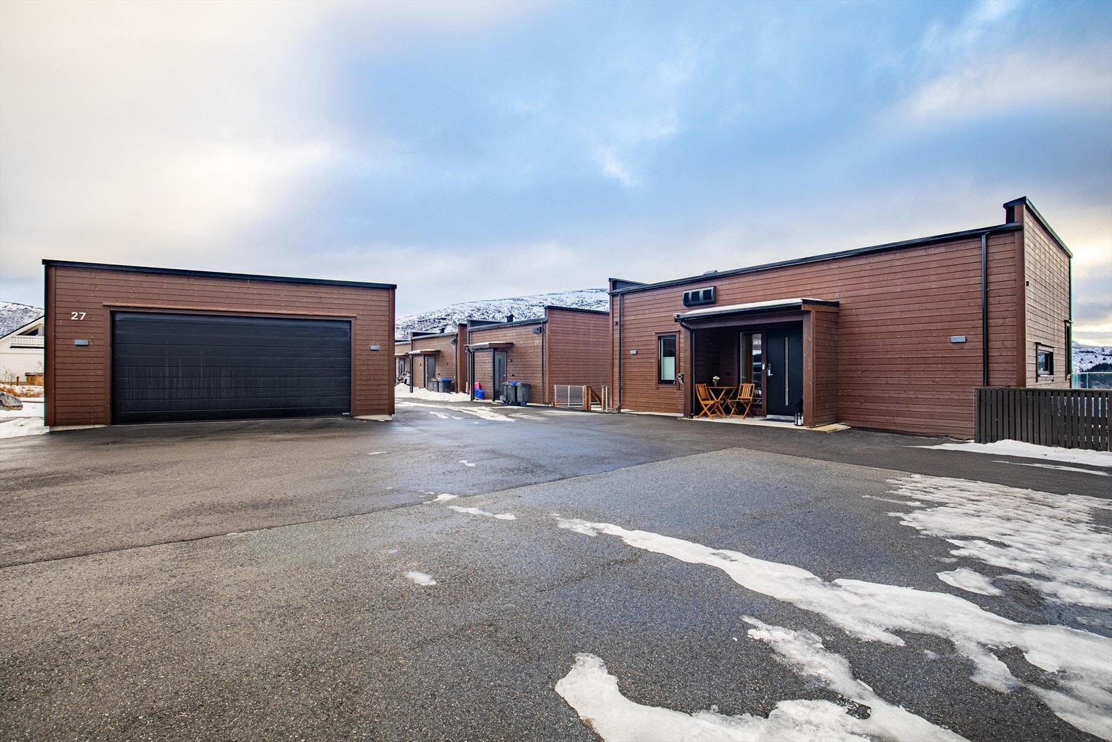 Fasade mot nord med stort asfaltert parkeringsområde, garasje og hovedinngang. Galleribilde