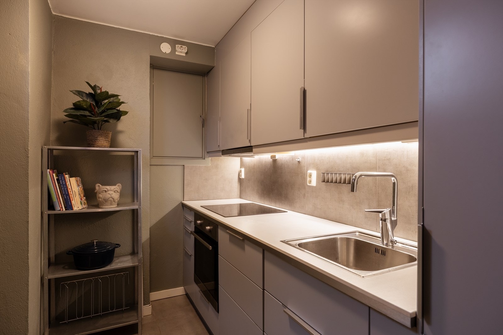 Hybelkjøkkenet har glatte fronter og en praktisk laminert benkeplate med nedfelt stålkum. Over benkeskapene er det fliser, og innredningen er komplett med integrert induksjonstopp, stekeovn, oppvaskmaskin og kjøl/frys. Galleribilde