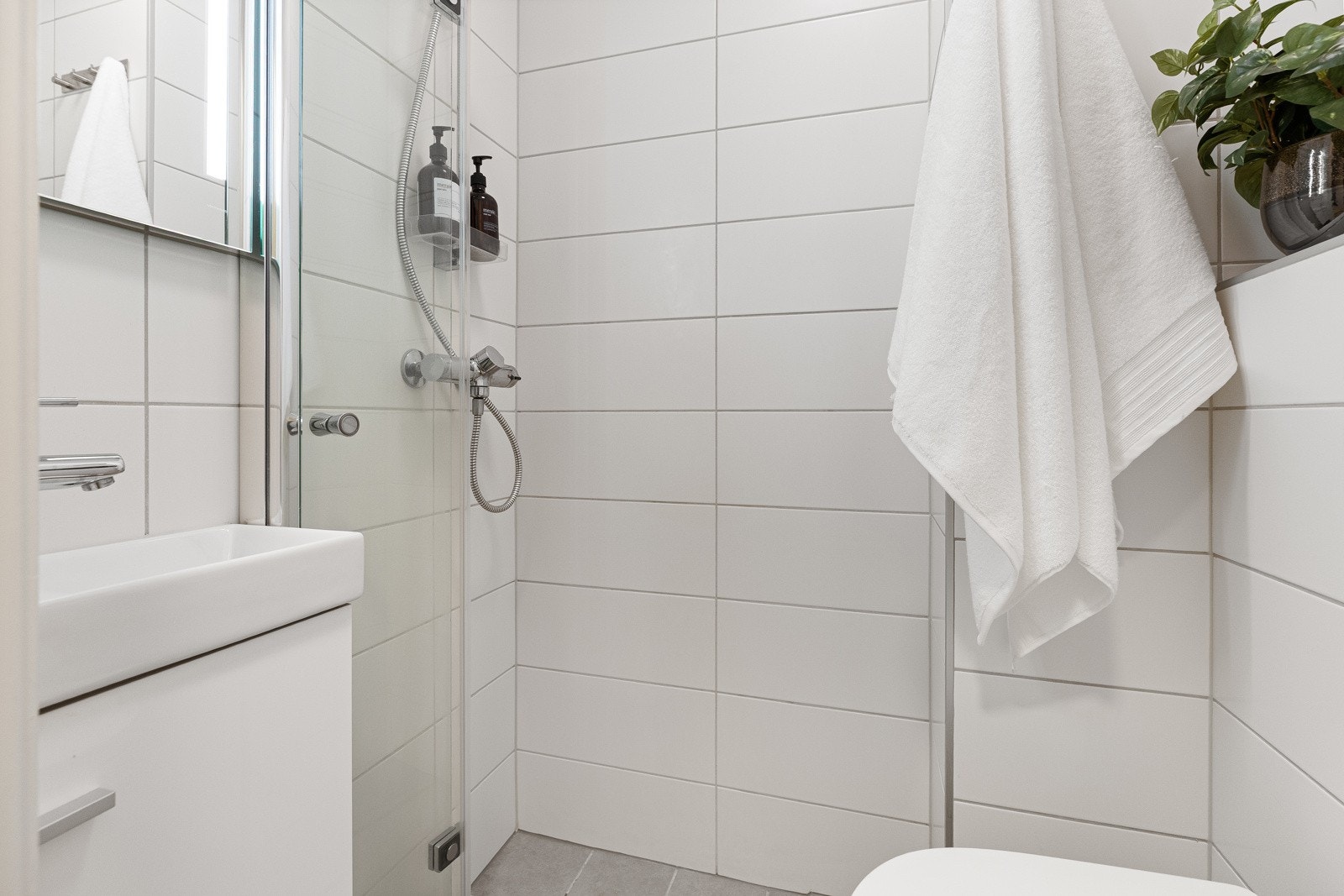 Badet har grå 20x20 cm fliser på gulv og hvite 20x50 cm fliser på vegger, med malt himling Galleribilde