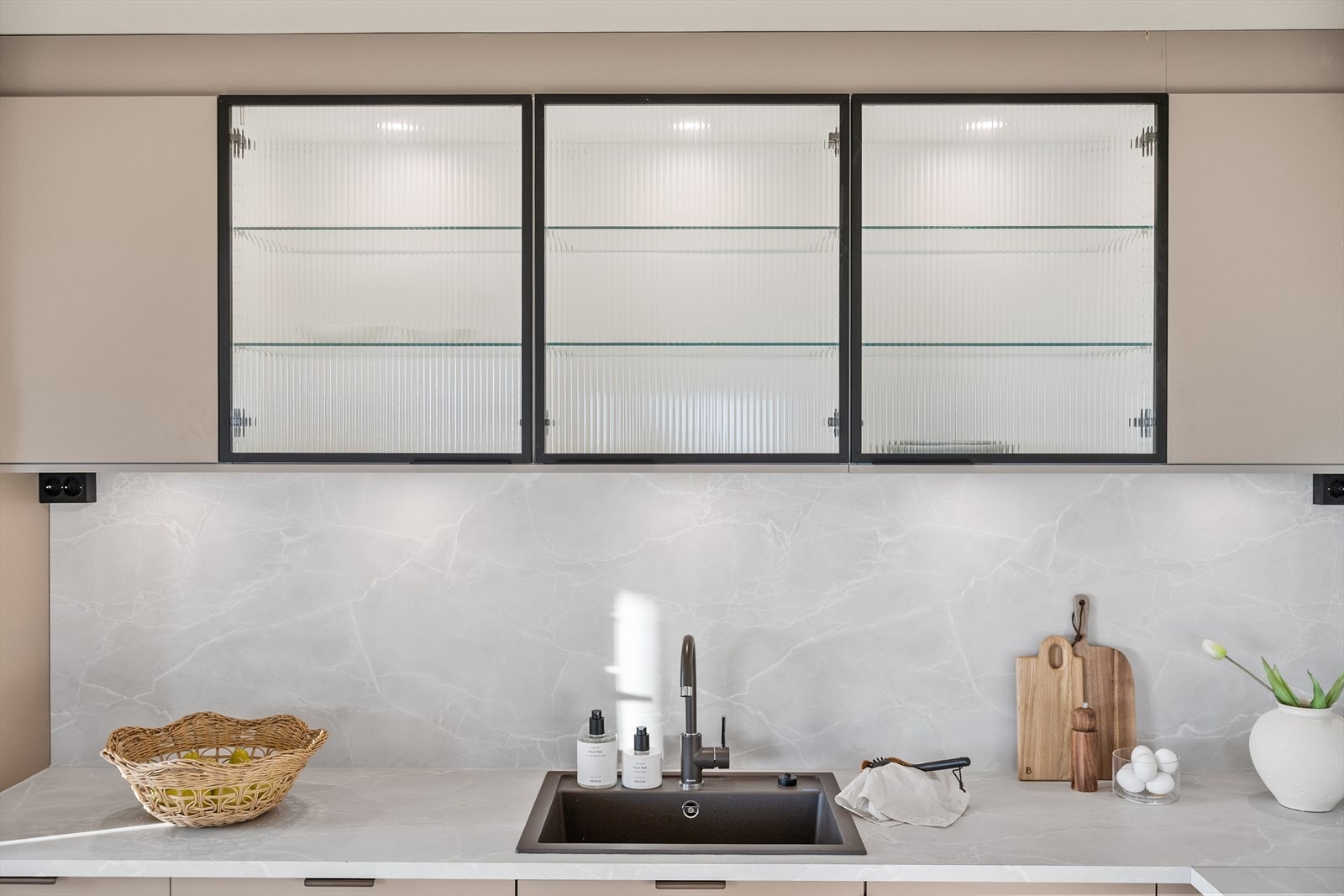 Overskapene med glassfronter og innvendig belysning tilfører et eksklusivt preg og gir både dekorativ og praktisk oppbevaring. Galleribilde