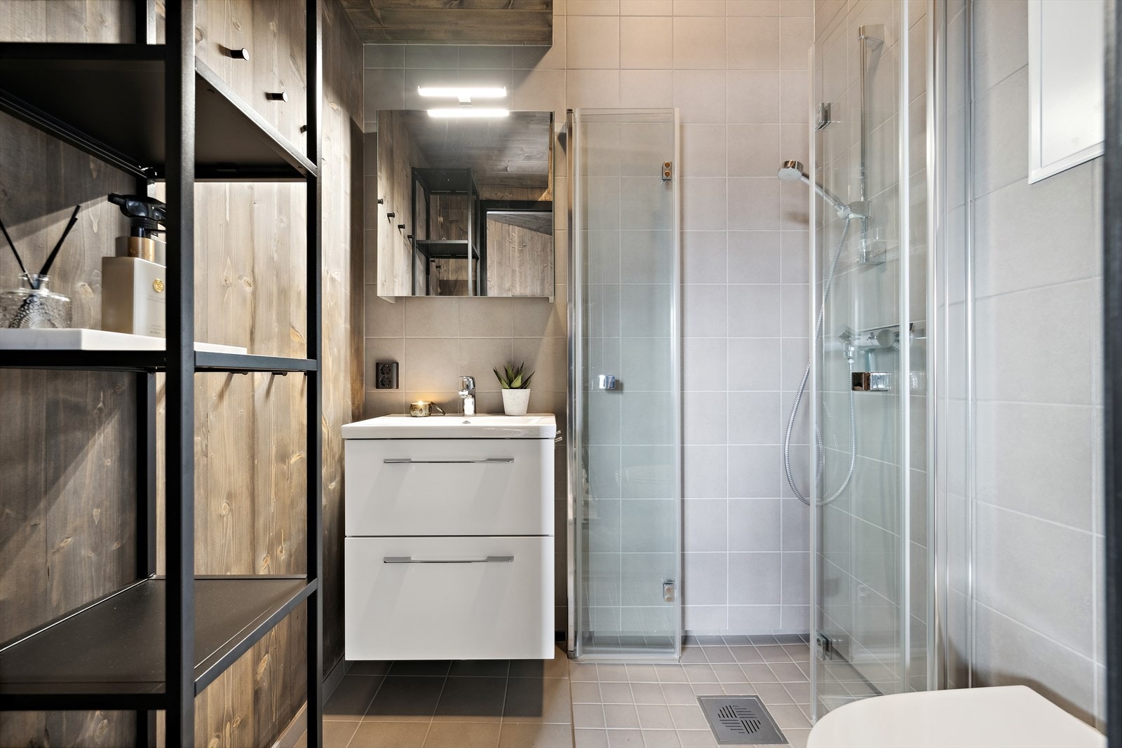 Lekkert delvis flislagt baderom med dusjhørne, servant på underskap og vegghengt toalett. Praktiske foldedører i herdet glass gir god plassutnyttelse. Galleribilde