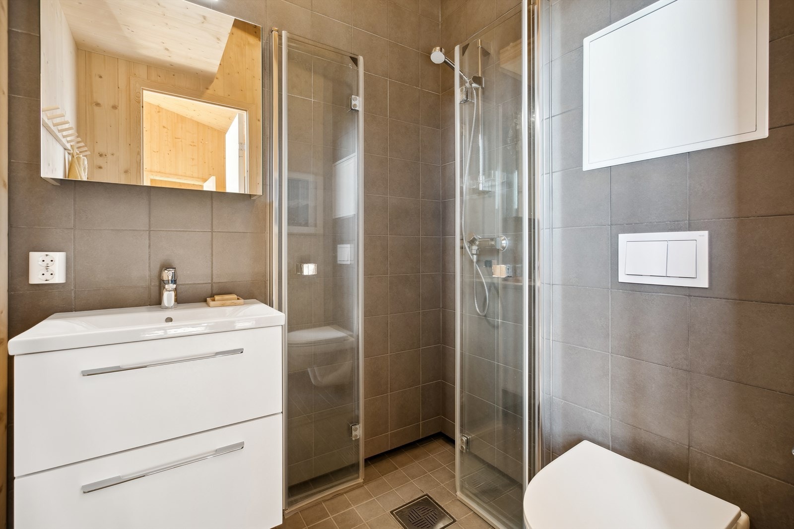 Lekkert delvis flislagt baderom med dusjhørne hvor man har innfellbare foldedører i herdet glass, tidløse flisvalg og gjennomførte detaljer. Galleribilde