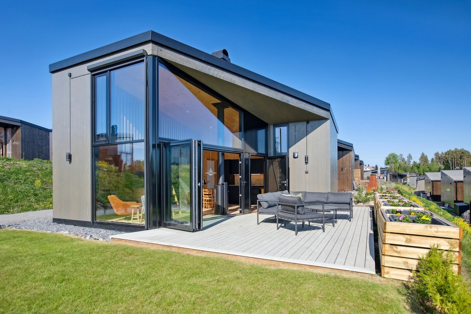 Hytta er godt vedlikeholdt og overflatebehandlet i en lys grå beis. Fine blomsterkasser skaper et naturlig skille mellom rekkene av hytter på feltet. Galleribilde