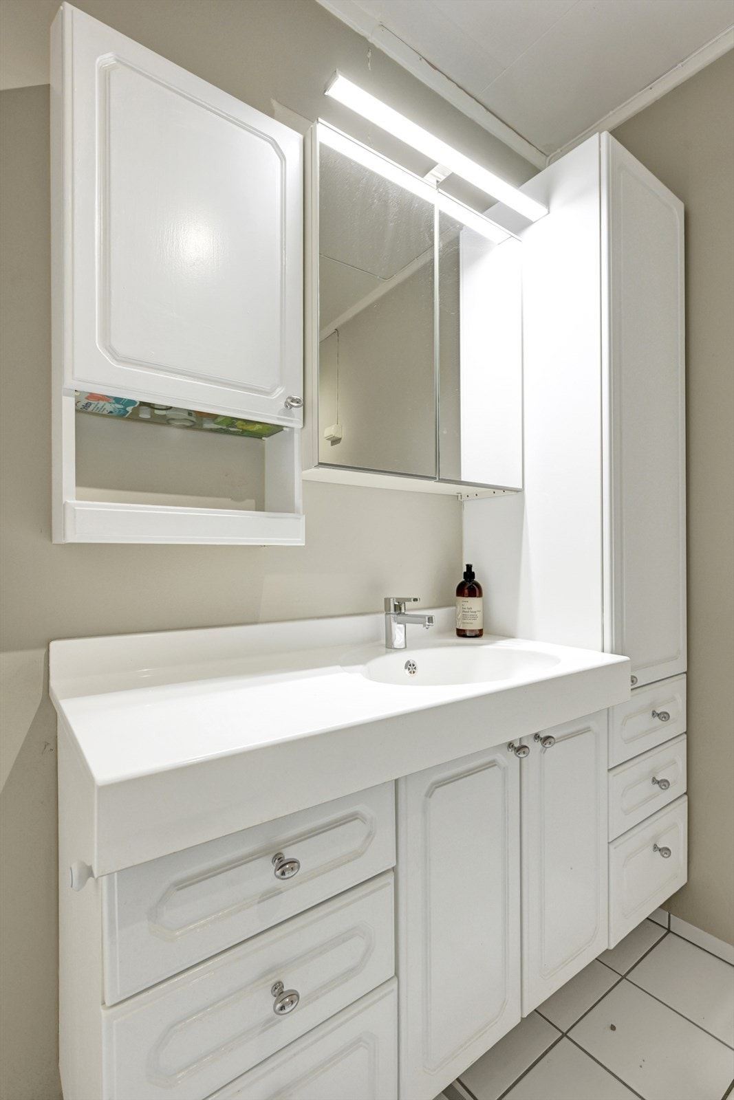 Innredet med heldekkende servant, speil og speilskap, gulvmontert toalett og baderomsinnredning med skuffer og skap. Galleribilde