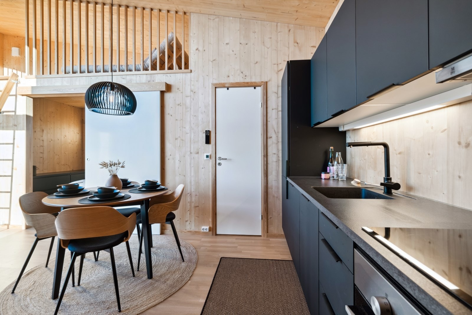 Fine kontraster med sort kjøkkeninnredning og hvite folierte dører, lys parkett og ubehandlet veggflater. Galleribilde