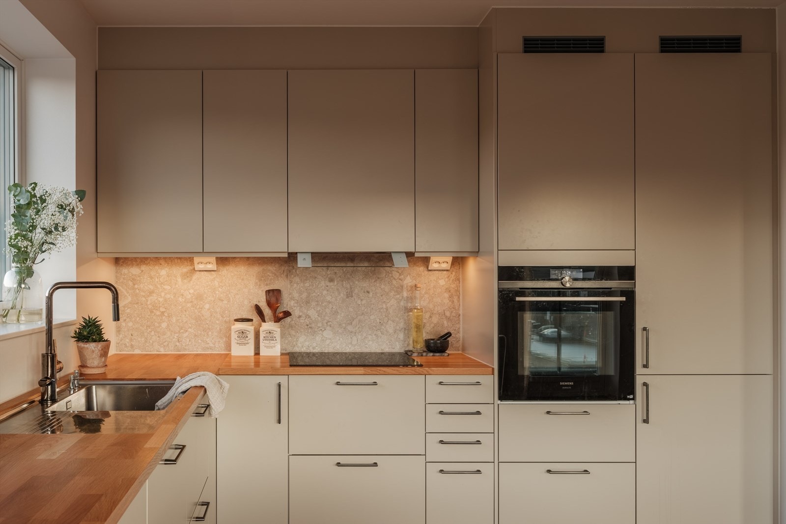 Videre er kjøkkenet utstyrt med integrerte hvitevarer som oppvaskmaskin, kjøl-/fryseskap, stekeovn og induksjonstopp, samt ventilator, komfyrvakt og god arbeidsbelysning. Galleribilde