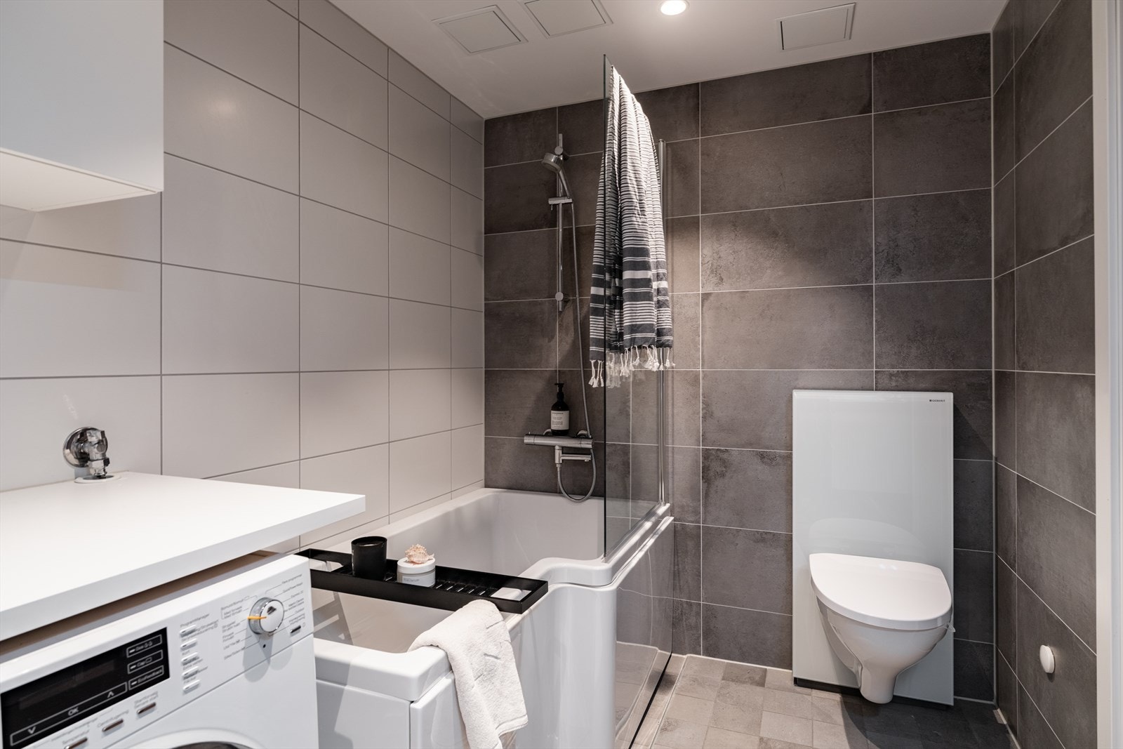 Badet er utstyrt med mekanisk avtrekk, vegghengt toalett og et badekar med veggmontert dusjarmatur. Galleribilde