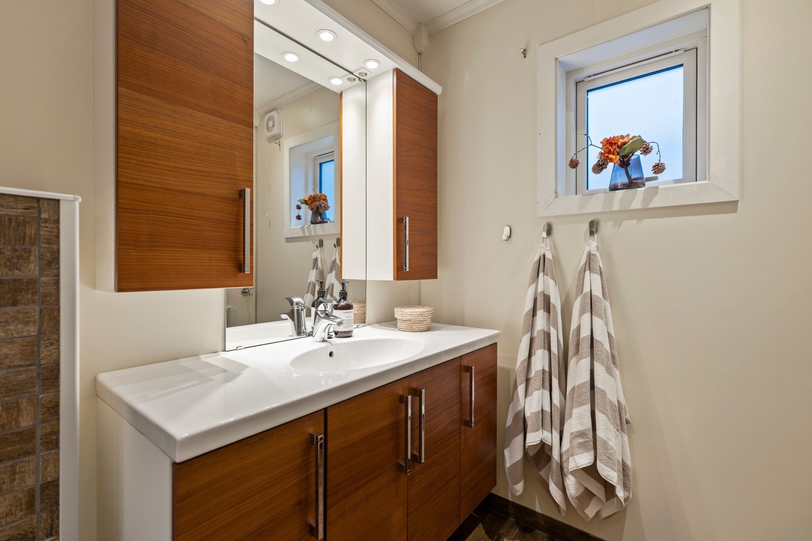 Rommet er innredet med vegghengt servantskap med heldekkende servant, ett-greps armatur og speil med overlys og oppbevaringsskap. Galleribilde