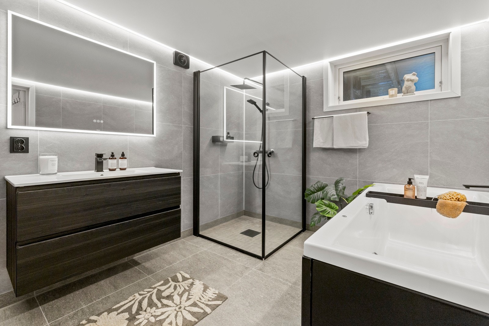 LED-listbelysning som gir en elegant og behagelig atmosfære. Badet er innredet med vegghengt servantskap med heldekkende servant og ett-greps armatur, speil med integrert lys, samt Galleribilde