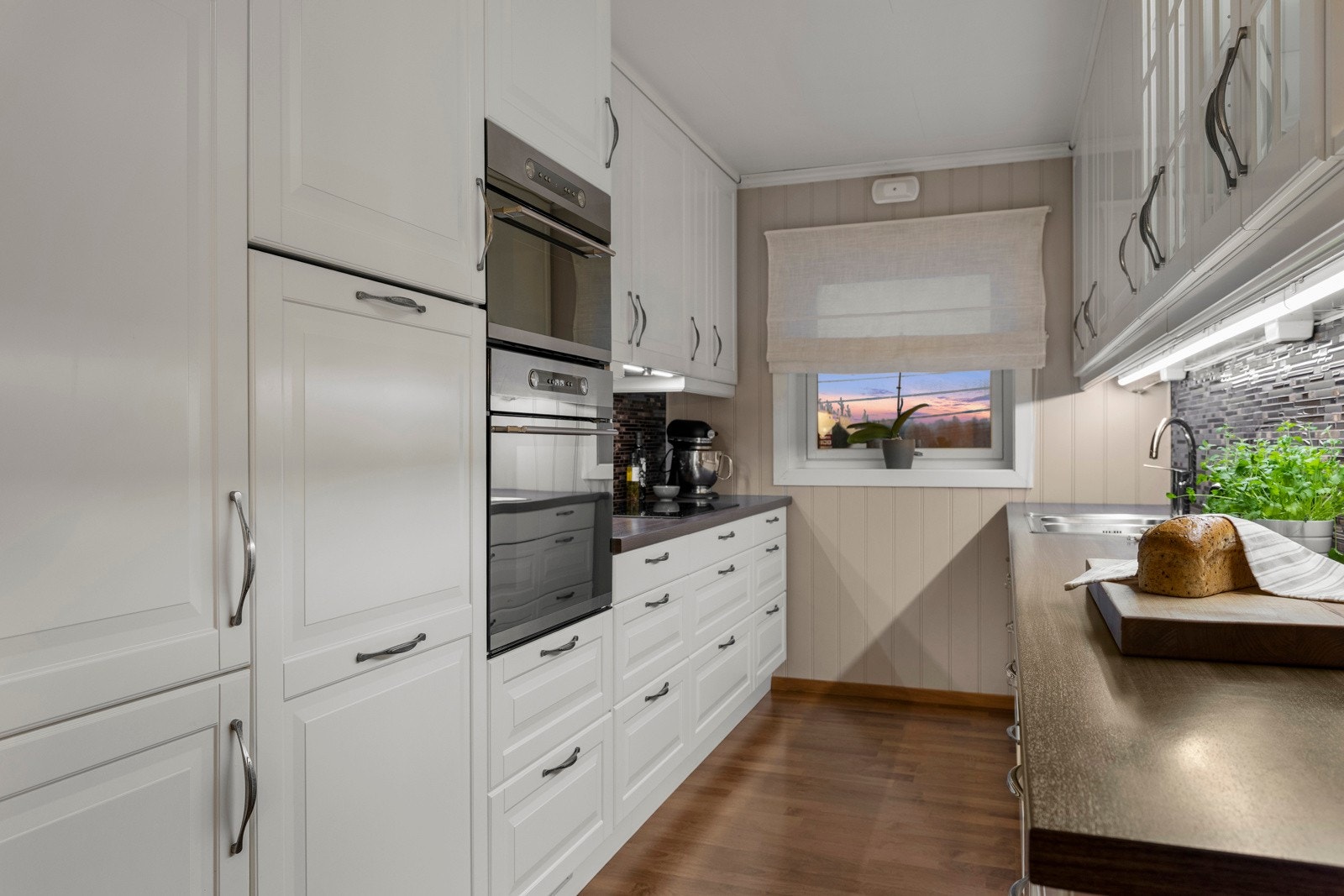 Under overskapene er det belysning som sikrer godt arbeidslys. Kjøkkenet er utstyrt med integrerte hvitevarer, inkludert kjøleskap med frysedel, stekeovn, mikrobølgeovn, induksjonstopp og oppvaskmaskin. Galleribilde