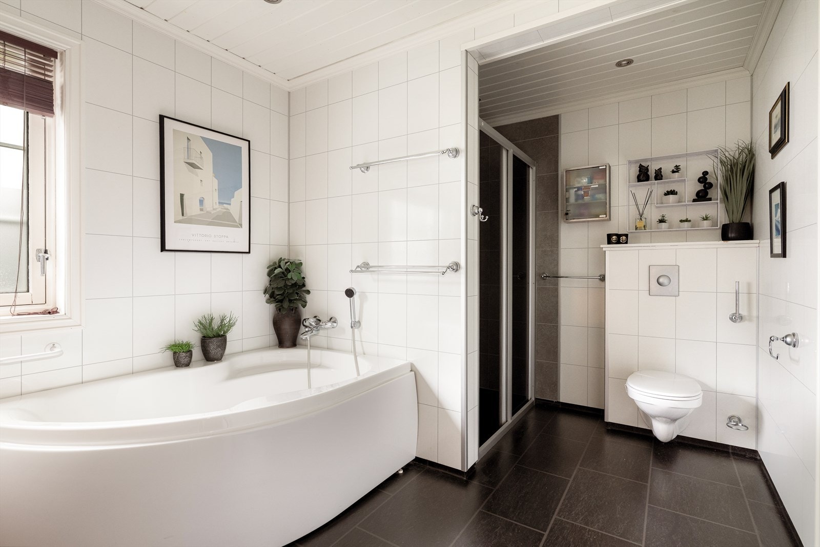 Badet er også innredet med dusjnisje, hjørnebadekar og veggmontert toalett. På veggoverflatene er det baderomsplater. Baderomspanel i dusjen ble byttet i 2021. Galleribilde